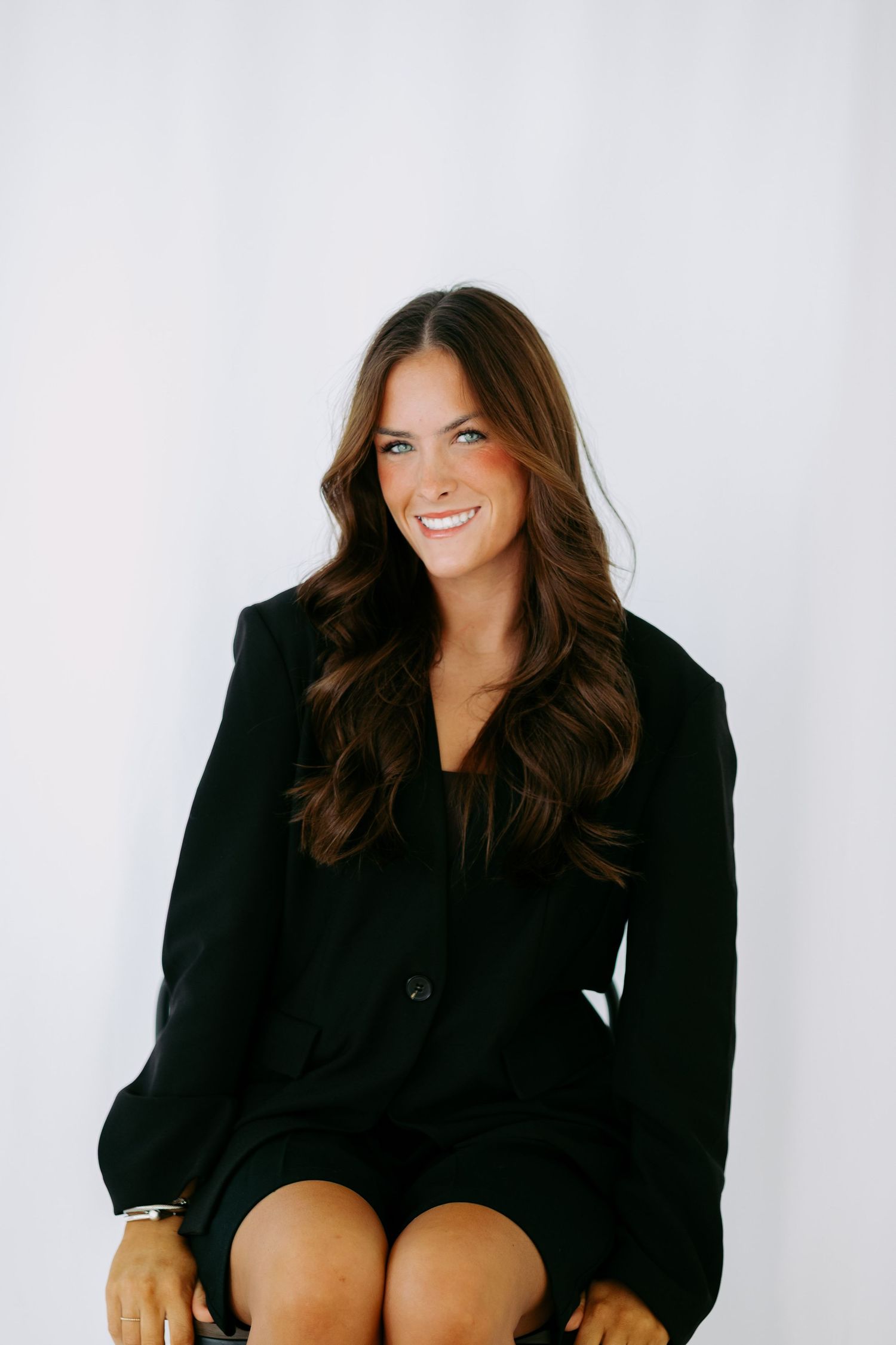 Professional headshot of a smiling brunette woman wearing a black blazer against a white background.