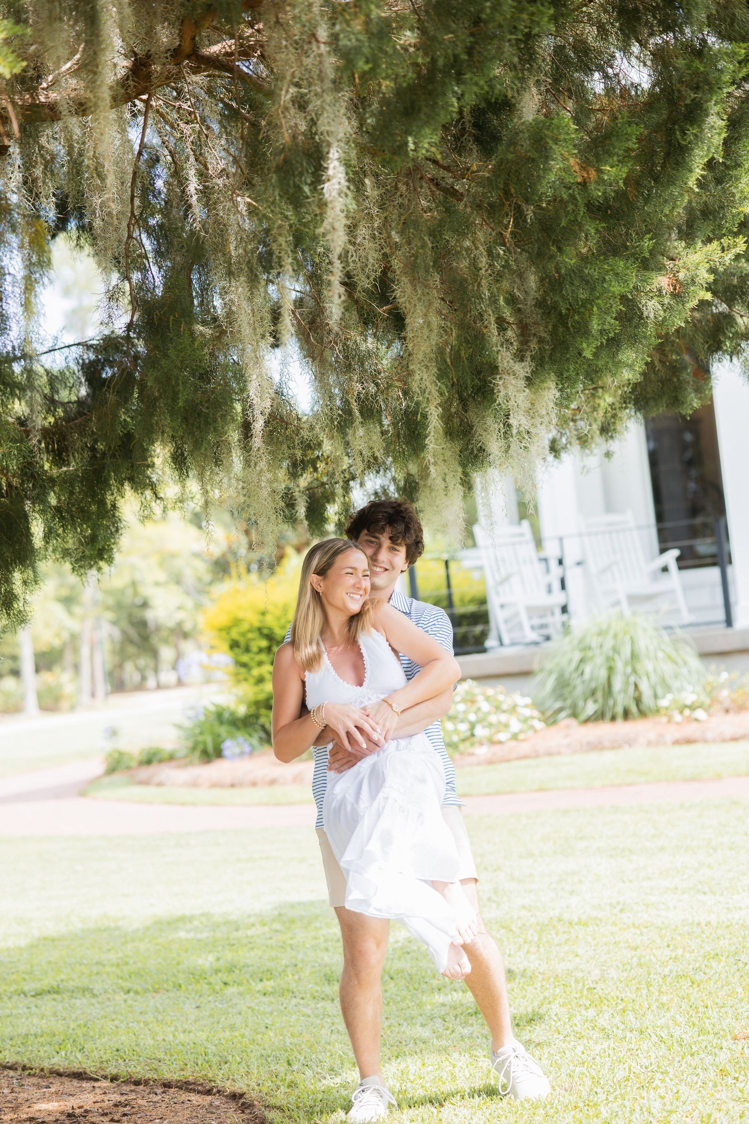 Happy couple embracing under a moss-draped tree in a sunny green garden setting.