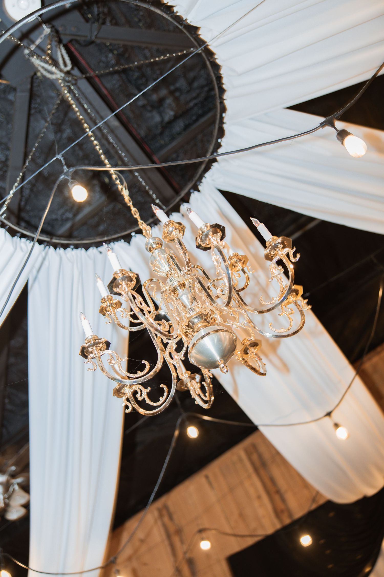Ornate crystal chandelier hanging from draped white fabric ceiling at elegant wedding reception venue.