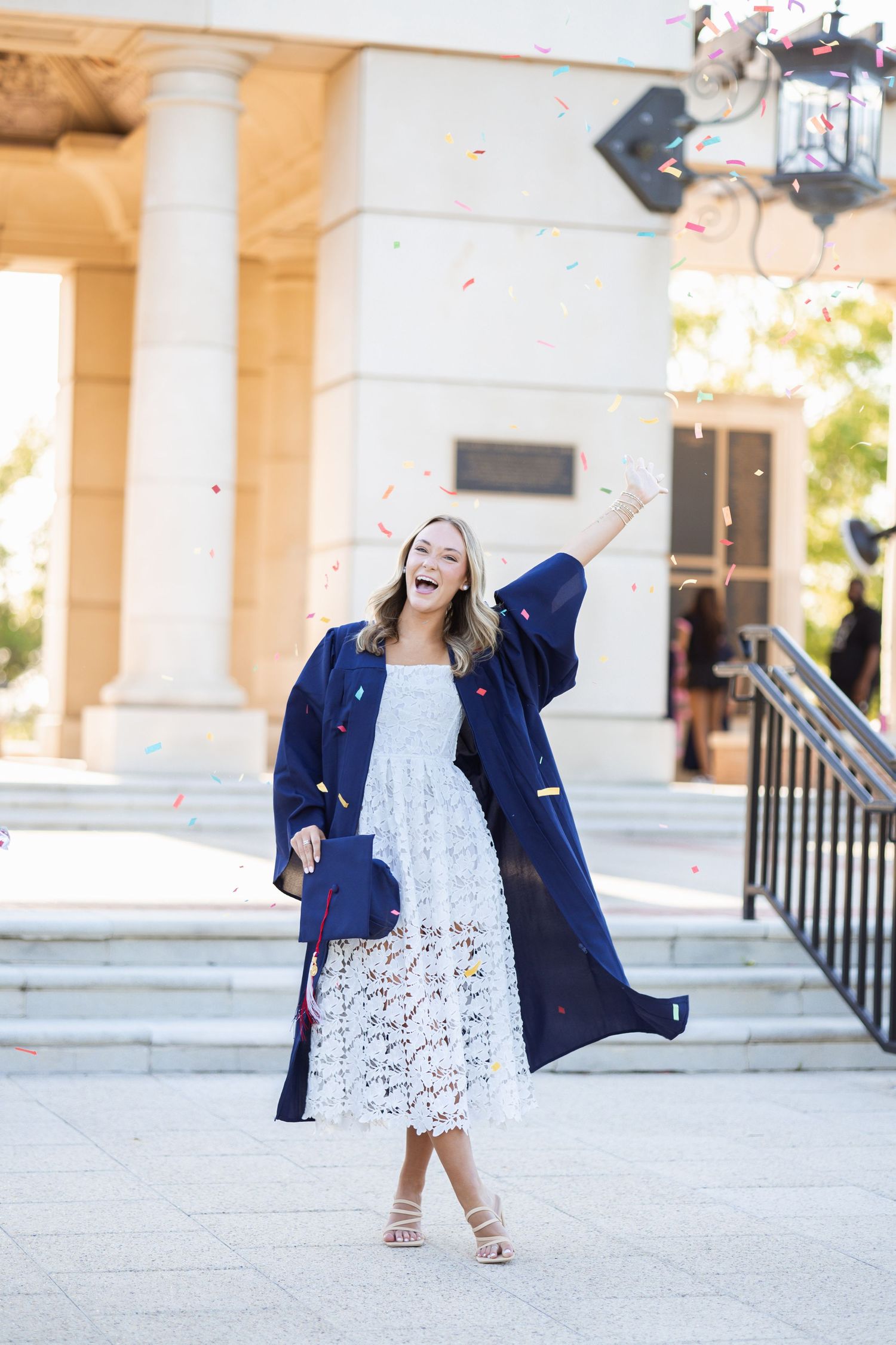 Joyful female graduate in navy robe celebrating with colorful confetti tossed in the air.