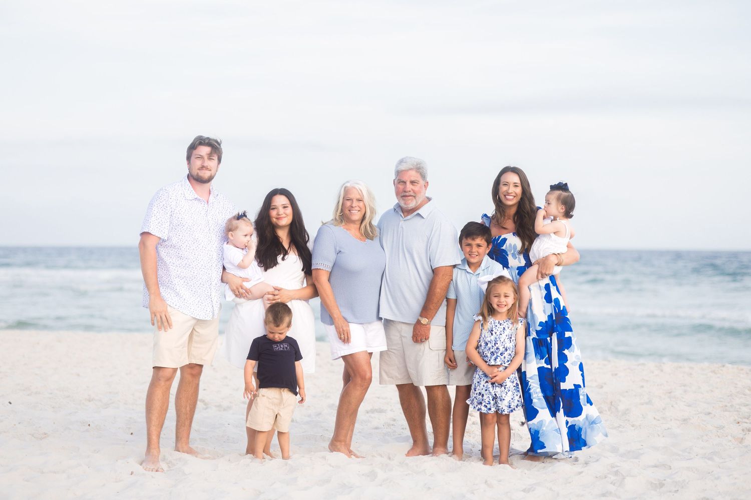 Extended multigenerational family posing together on a white sandy beach with calm ocean in the background.