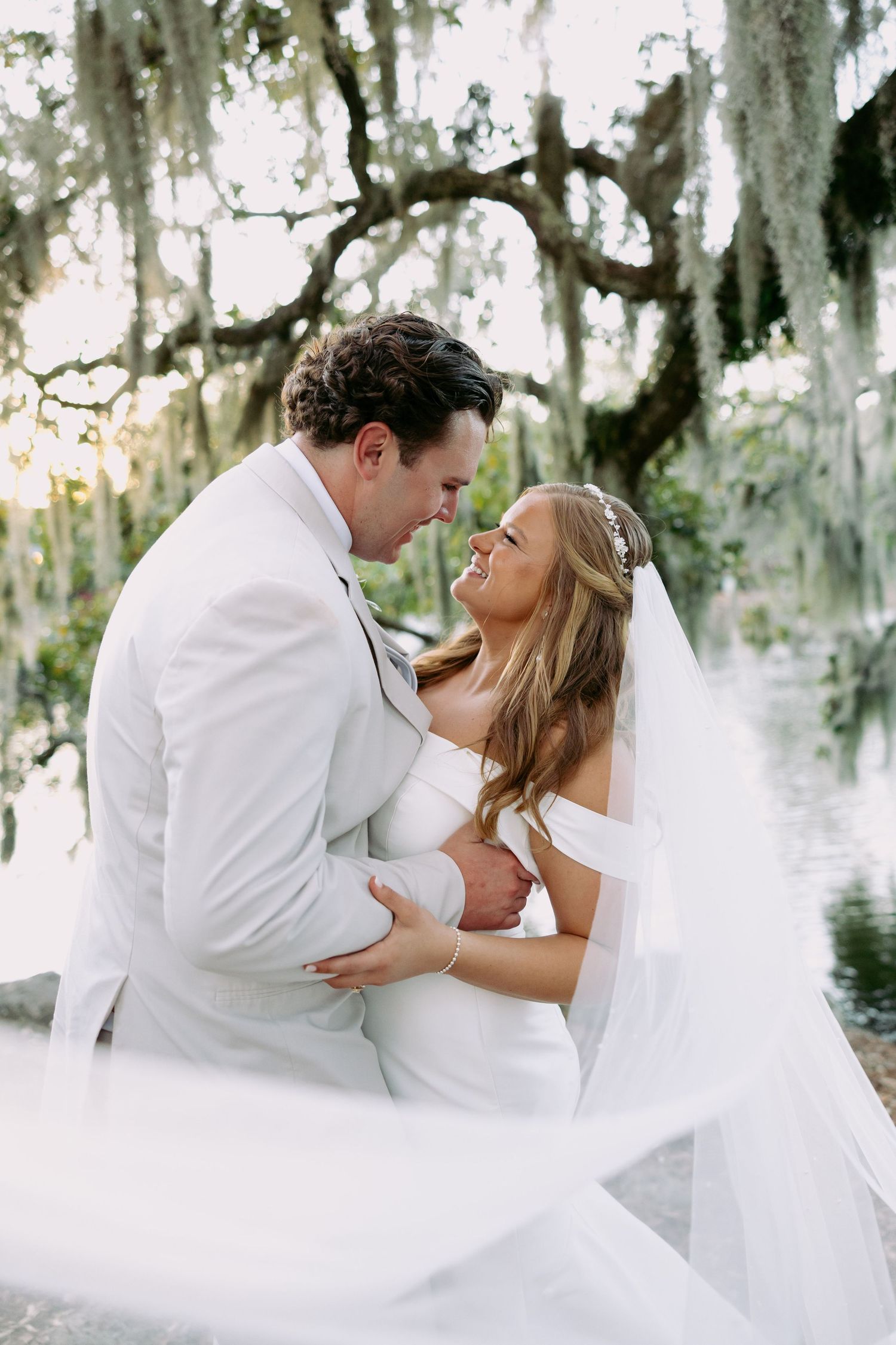 Bride and groom gazing at each other romantically under Spanish moss-draped oak trees with veil flowing.