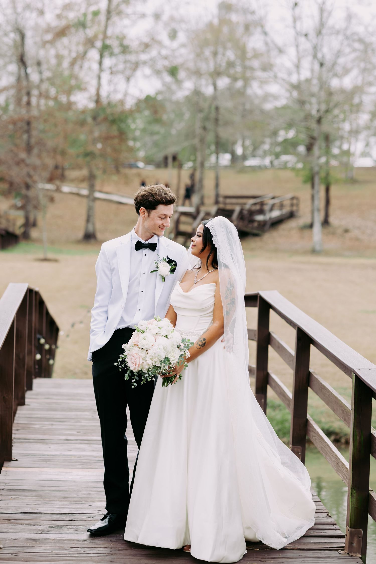 Bride and groom share a romantic moment on a wooden bridge at an outdoor wedding venue.