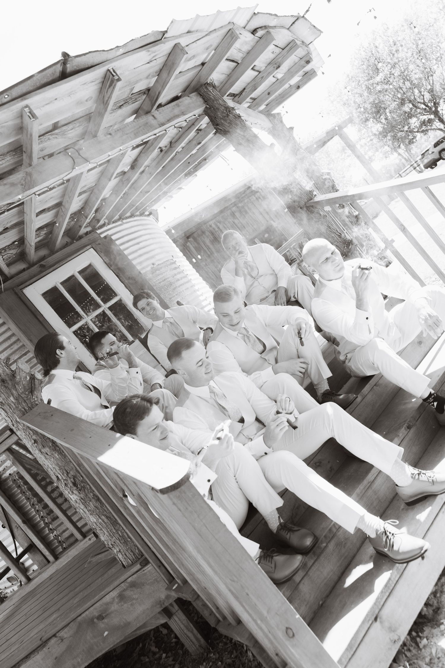 Black and white photo of groomsmen relaxing together on rustic wooden porch steps before wedding.