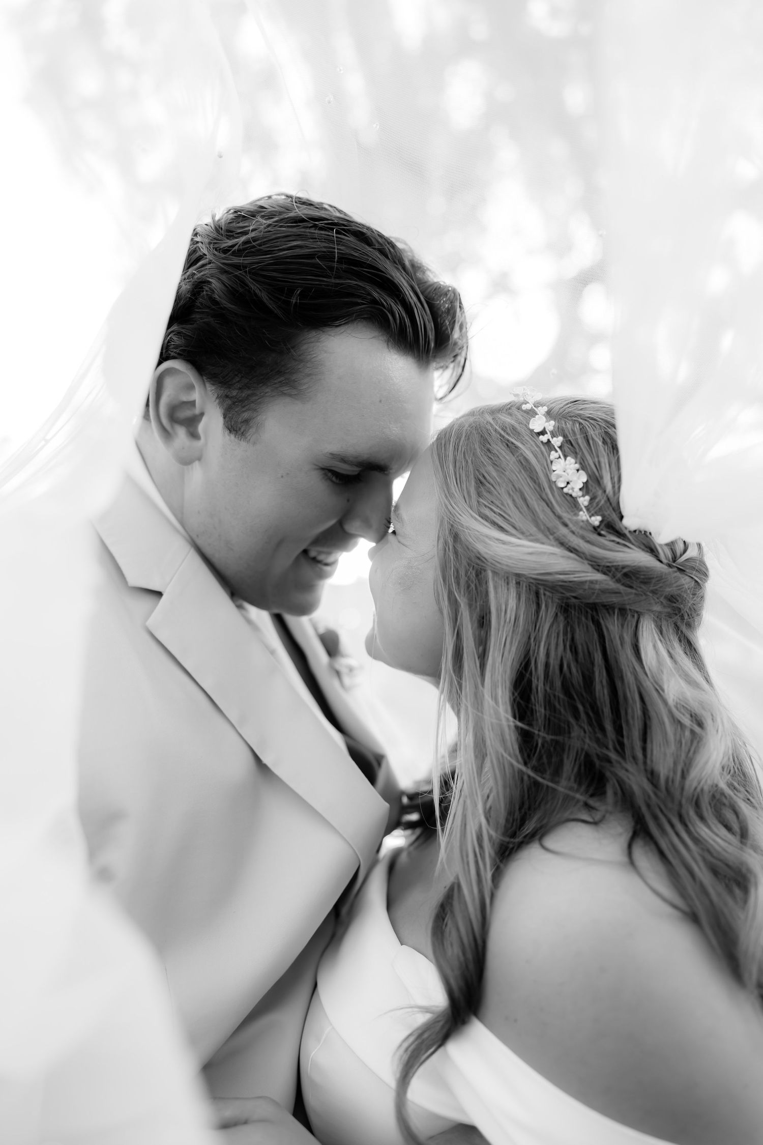 Romantic black and white portrait of bride and groom nearly kissing under a flowing veil.