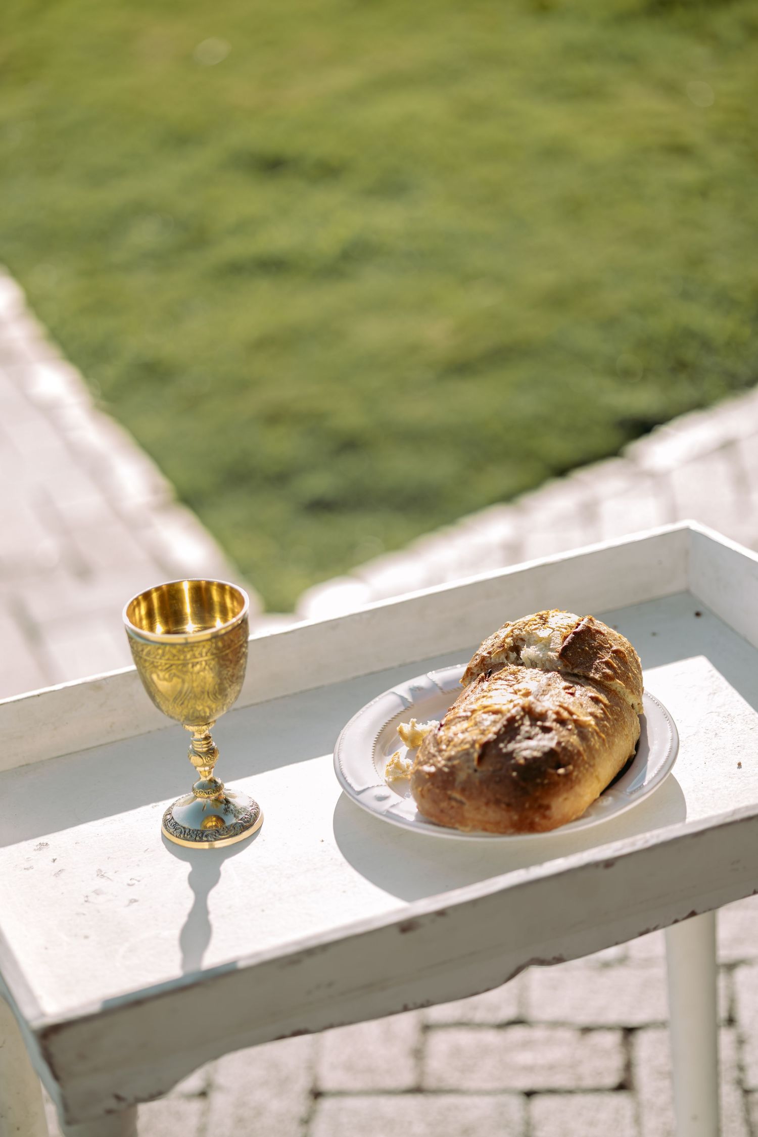 Gold chalice and bread on white table outdoors for wedding communion ceremony in sunlight.