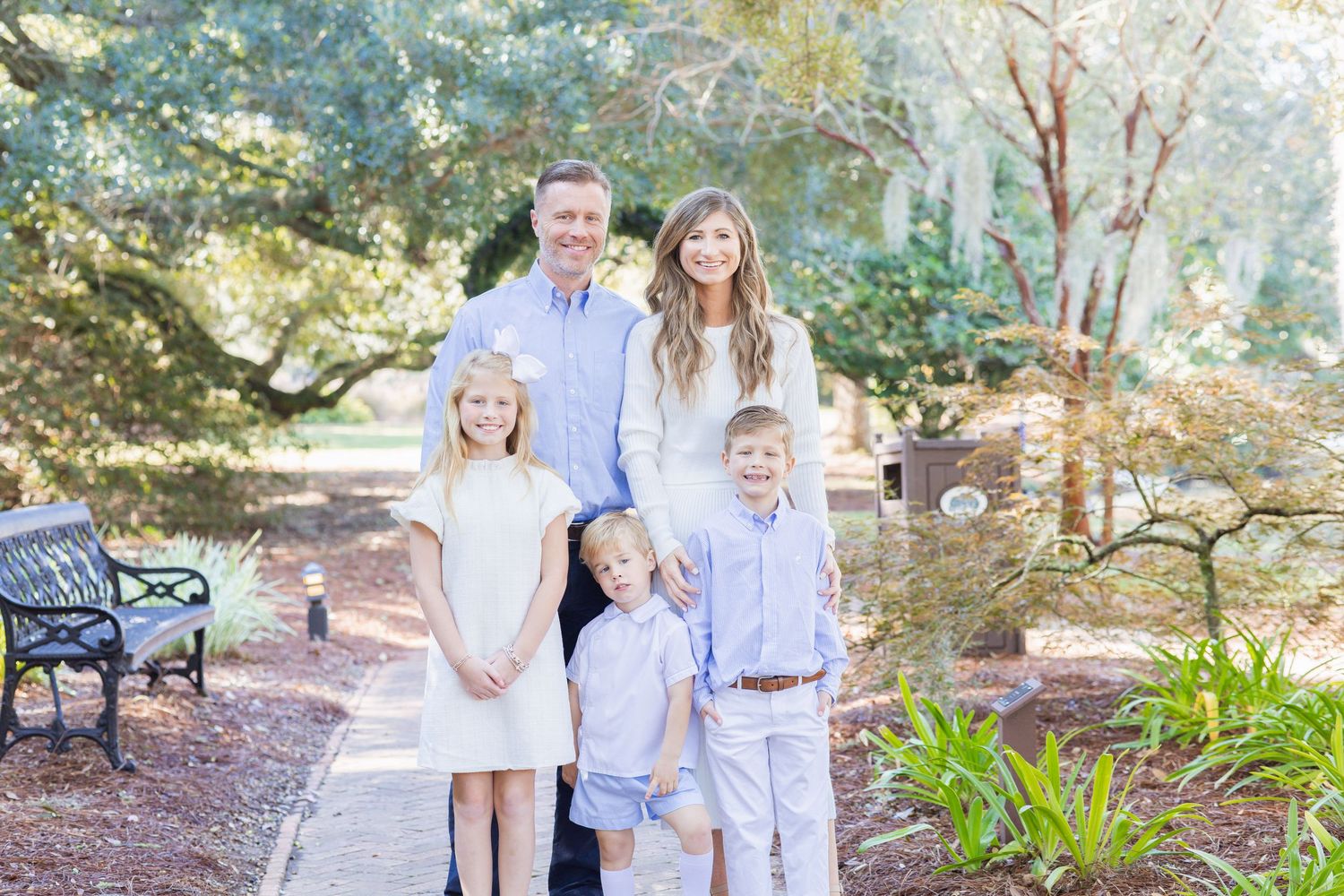 Happy family of five posing together in a lush green park setting for a portrait.