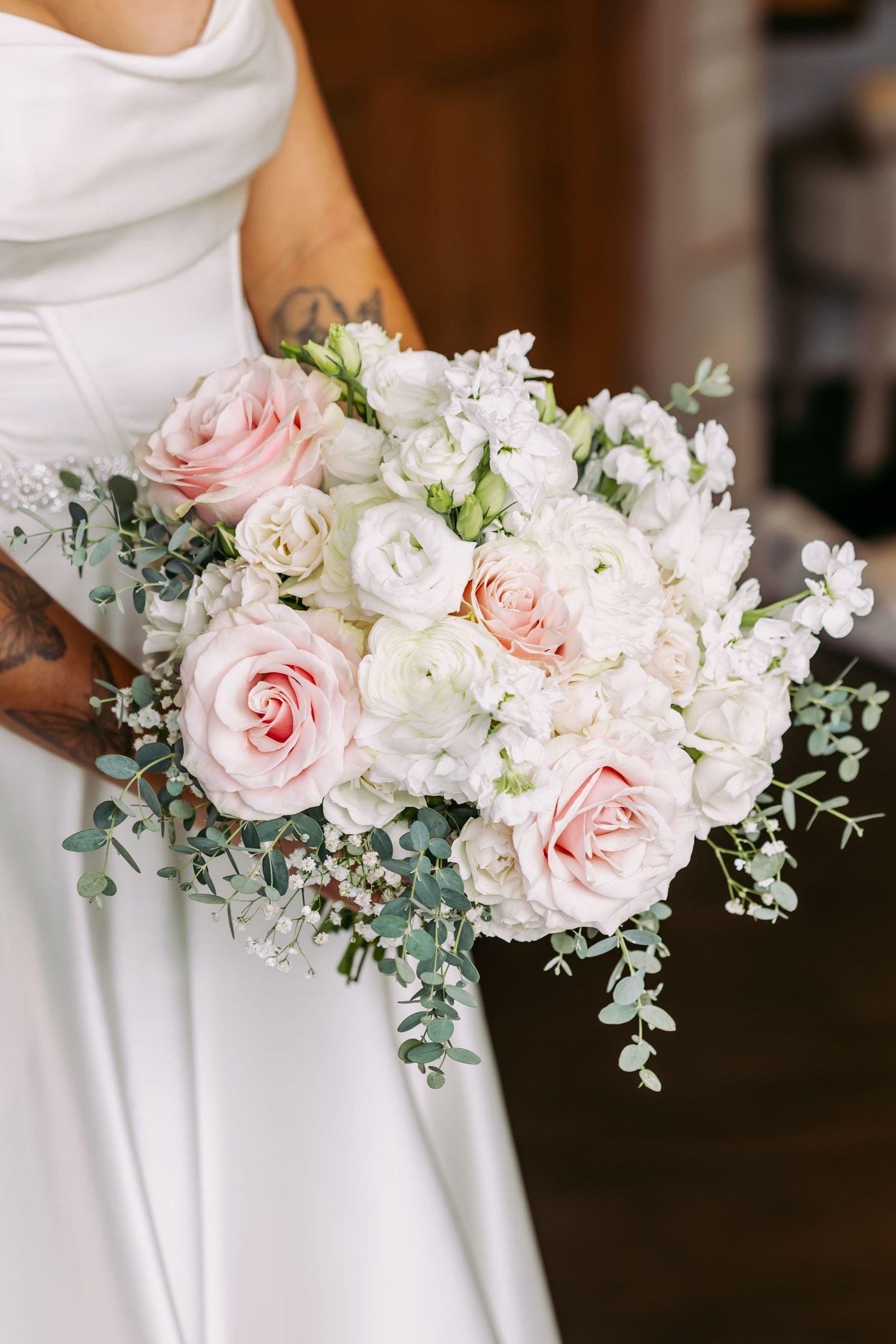 Bride holding lush bridal bouquet of blush pink roses, white ranunculus, and eucalyptus greenery.