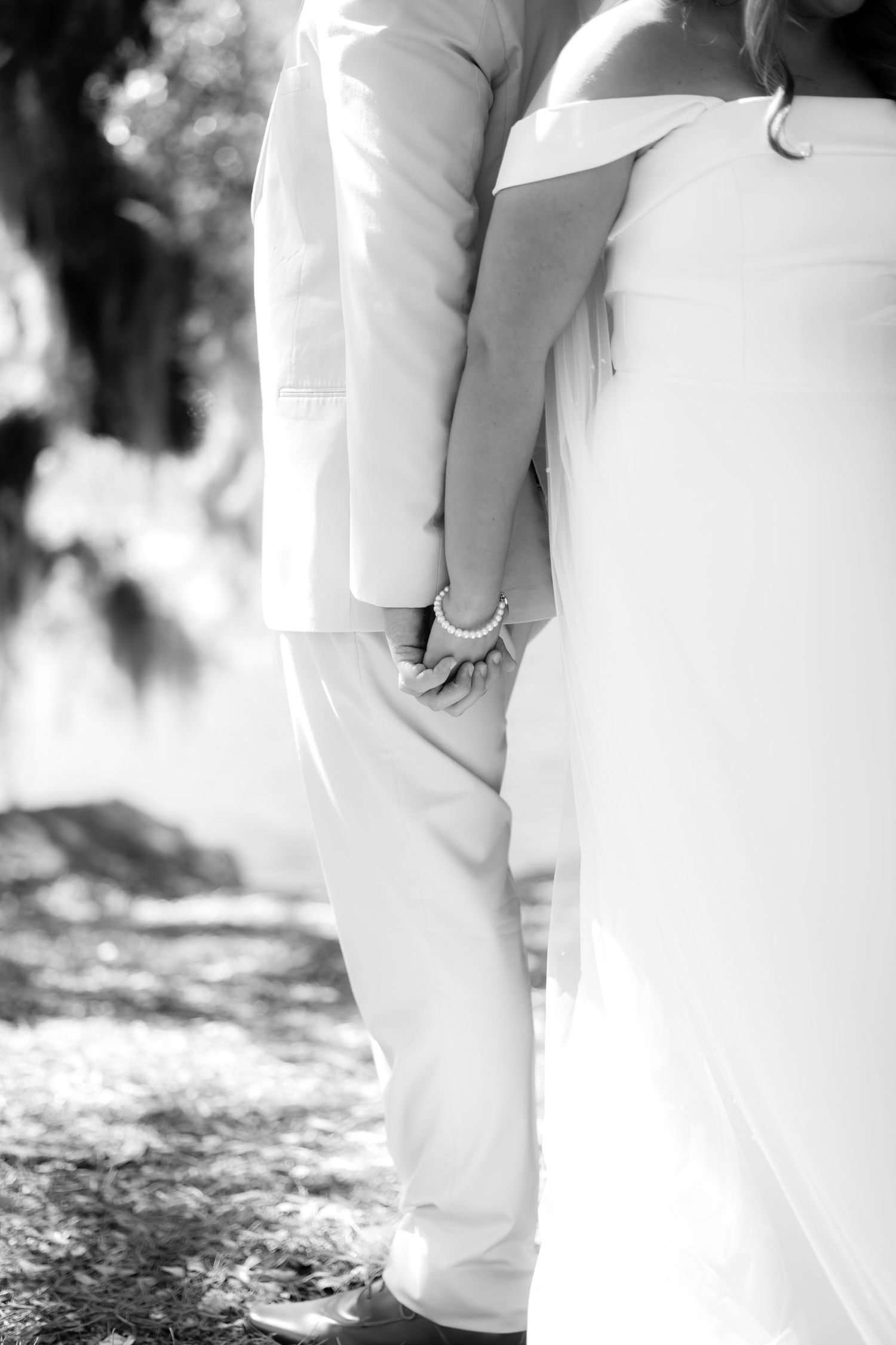 Black and white photo of bride and groom holding hands outdoors in a wooded setting.