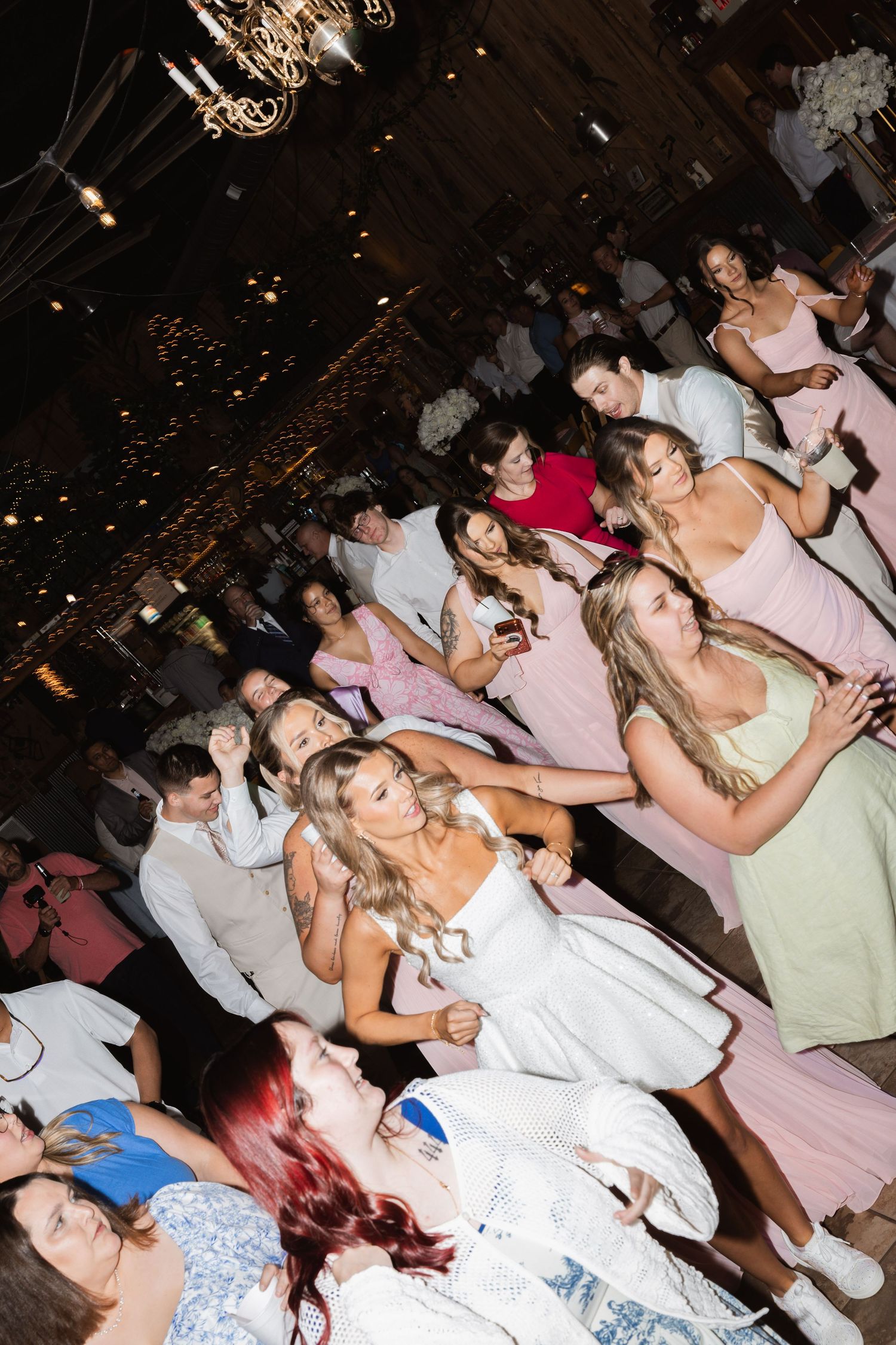 Bride tosses bouquet to excited crowd of guests on the wedding reception dance floor.