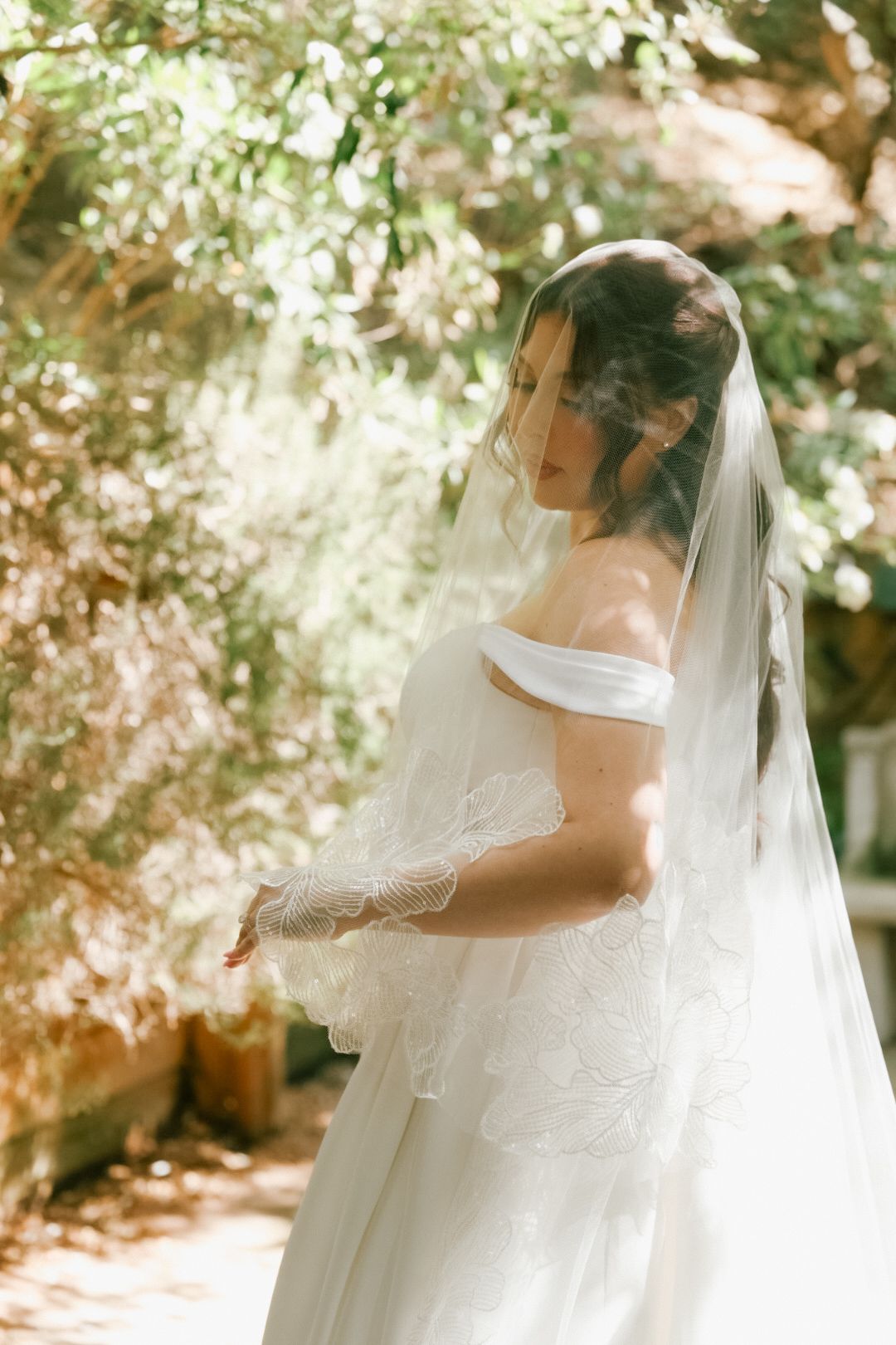 A bride standing in golden hour light with her sheer lace wedding veil covering her face.