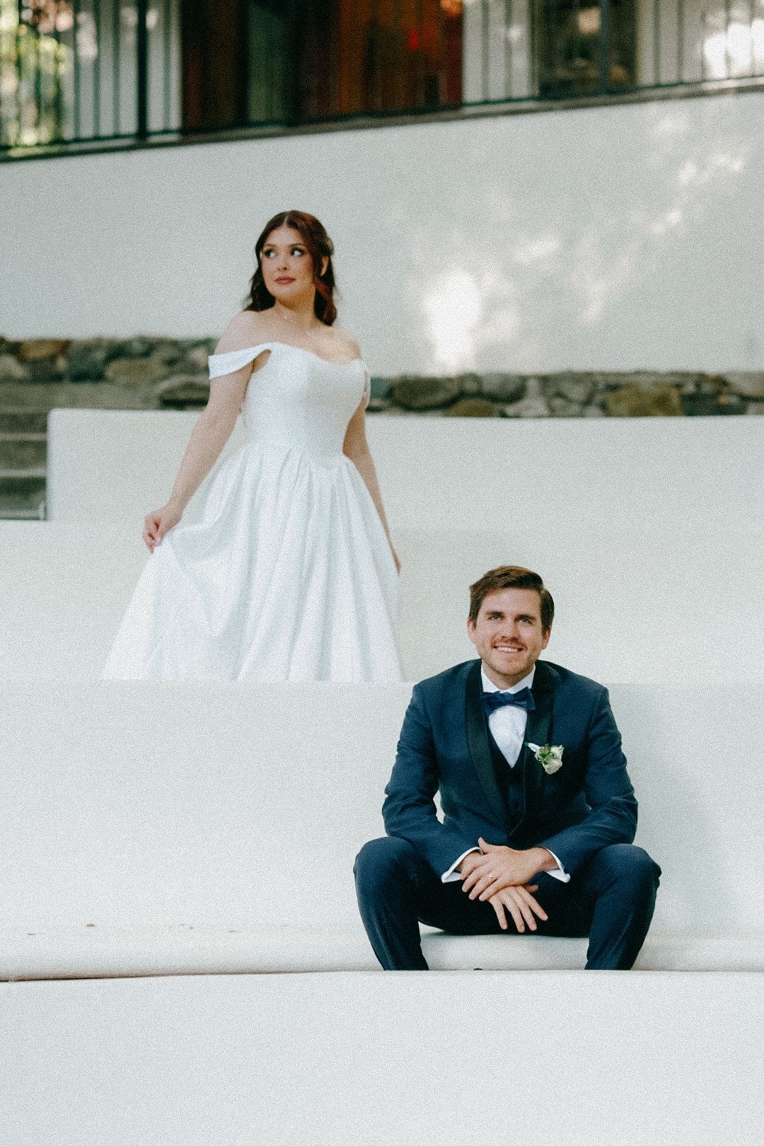 A bride standing on the tiers and a groom sitting on the white amphitheater steps at The 1909 wedding venue.