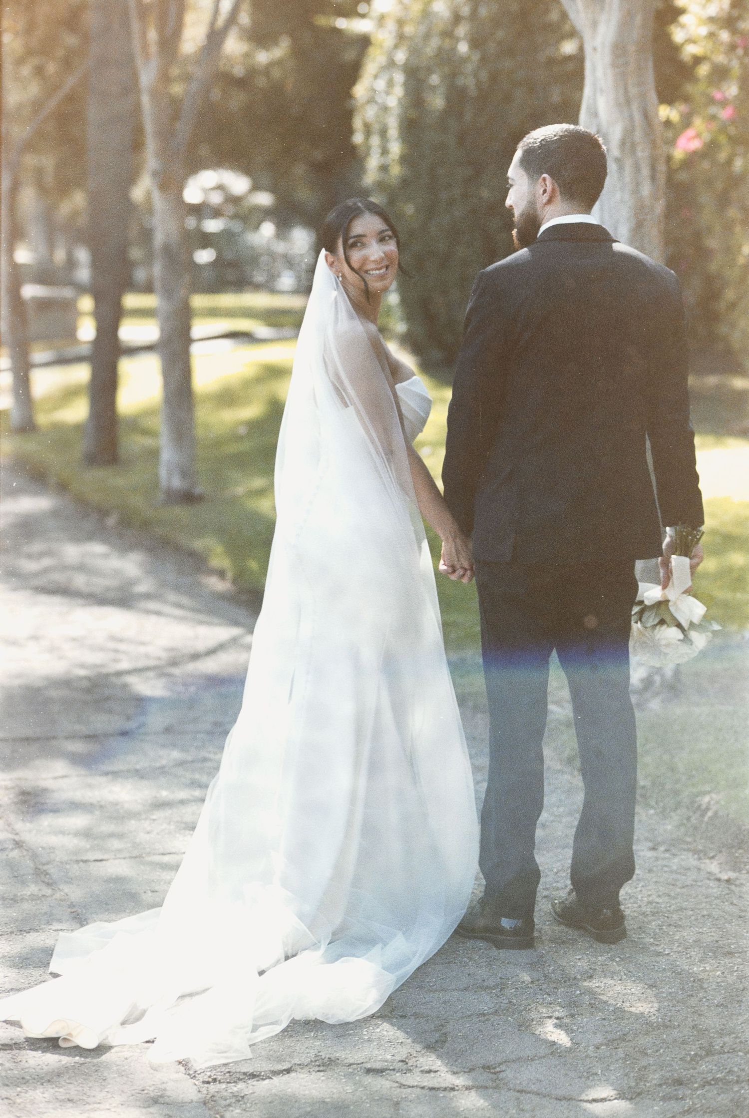 A bride looking over her shoulder while holding hands with her groom, captured by a Los Angeles film wedding photographer.