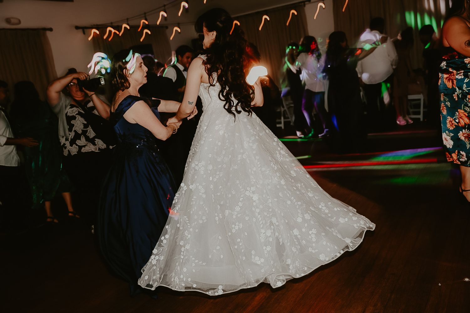 A bride dancing with guests under colorful reception lights at a Los Angeles wedding.