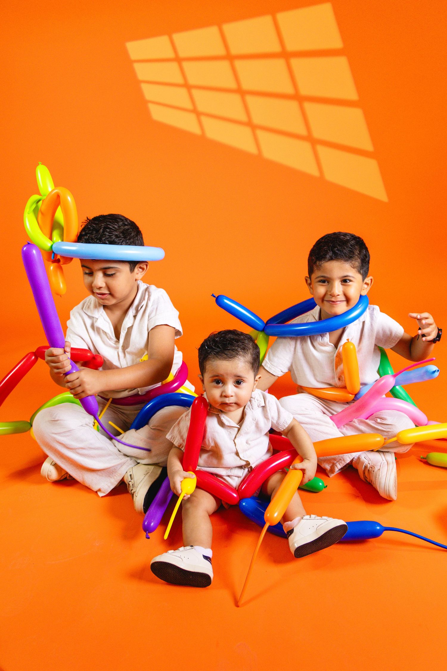 Three young children playing with colorful balloon animals on an orange background in a fun studio photo shoot.