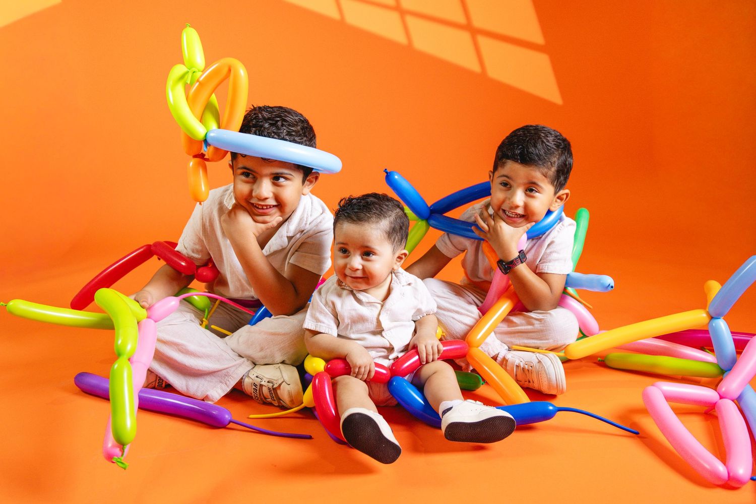 Three happy children playing with colorful balloon animals on an orange background.