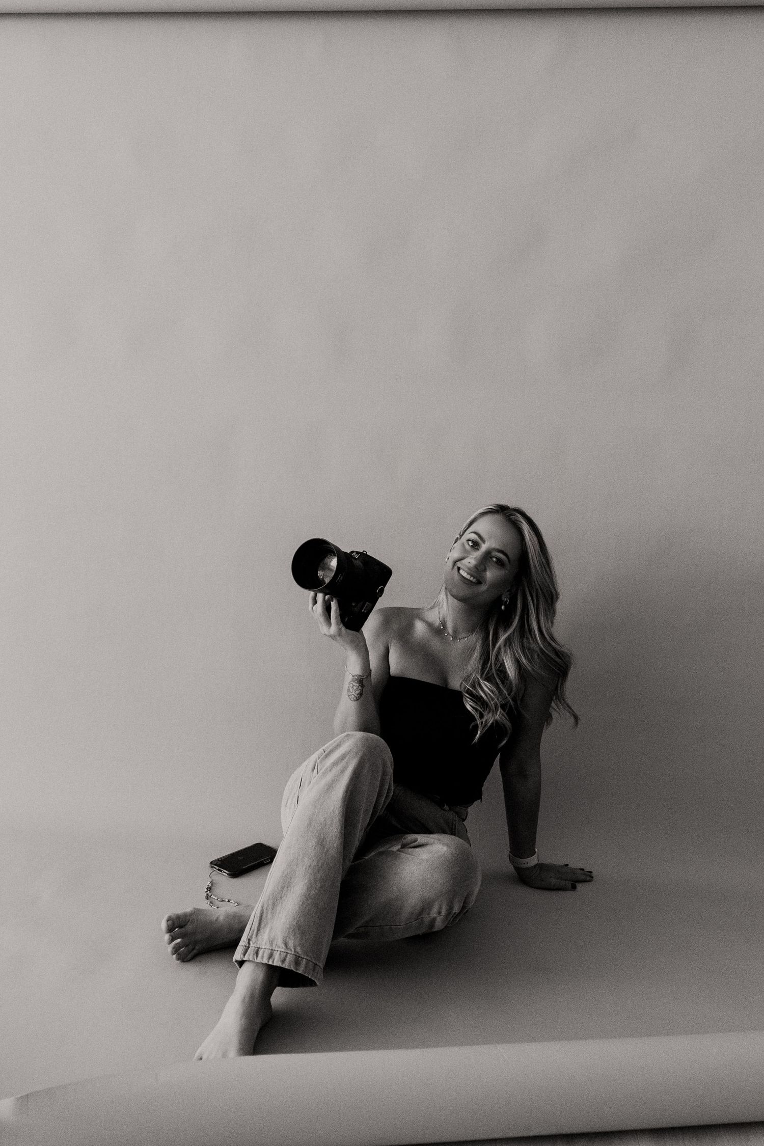 Black and white portrait of a photographer holding camera while sitting in a casual pose.