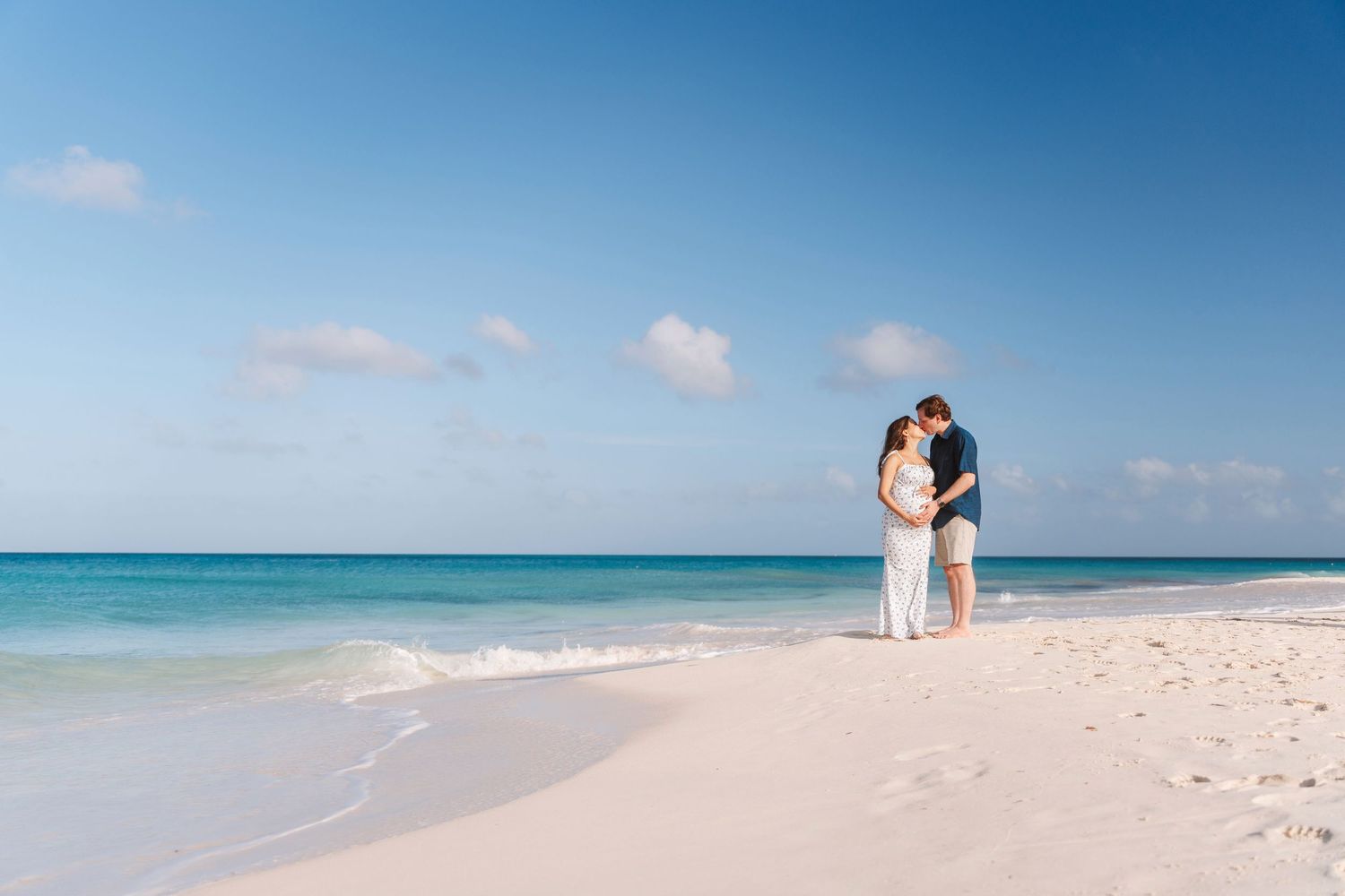 Couple embracing on a pristine white sand beach with turquoise ocean water and clear blue sky.