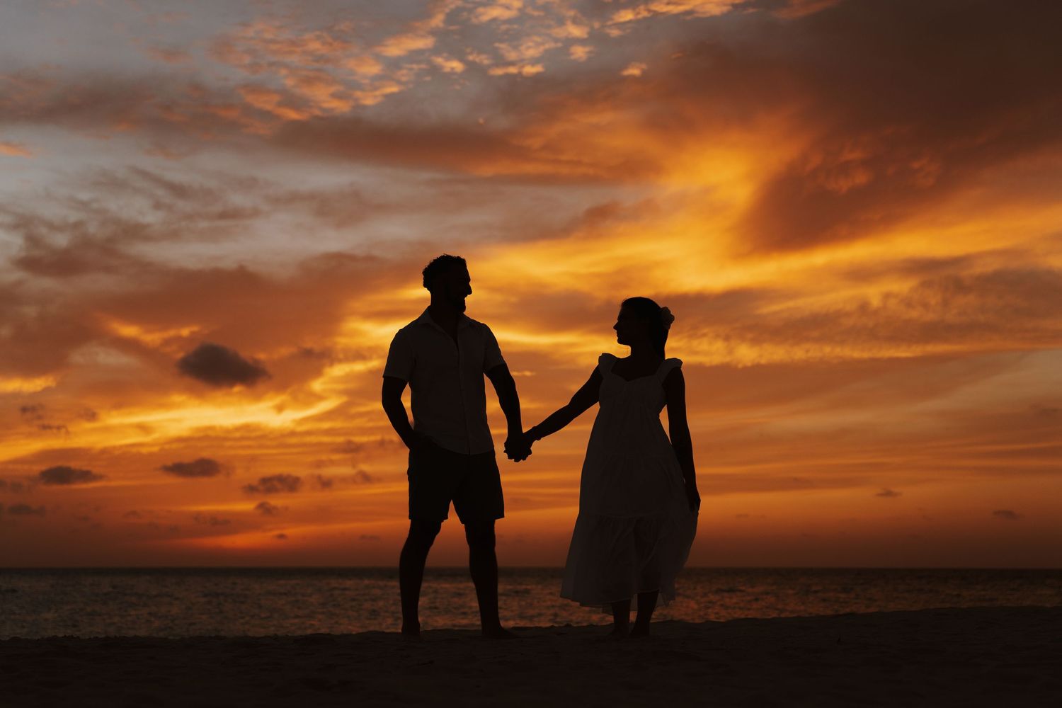 Silhouettes of people standing against a dramatic orange and red sunset sky over the horizon.
