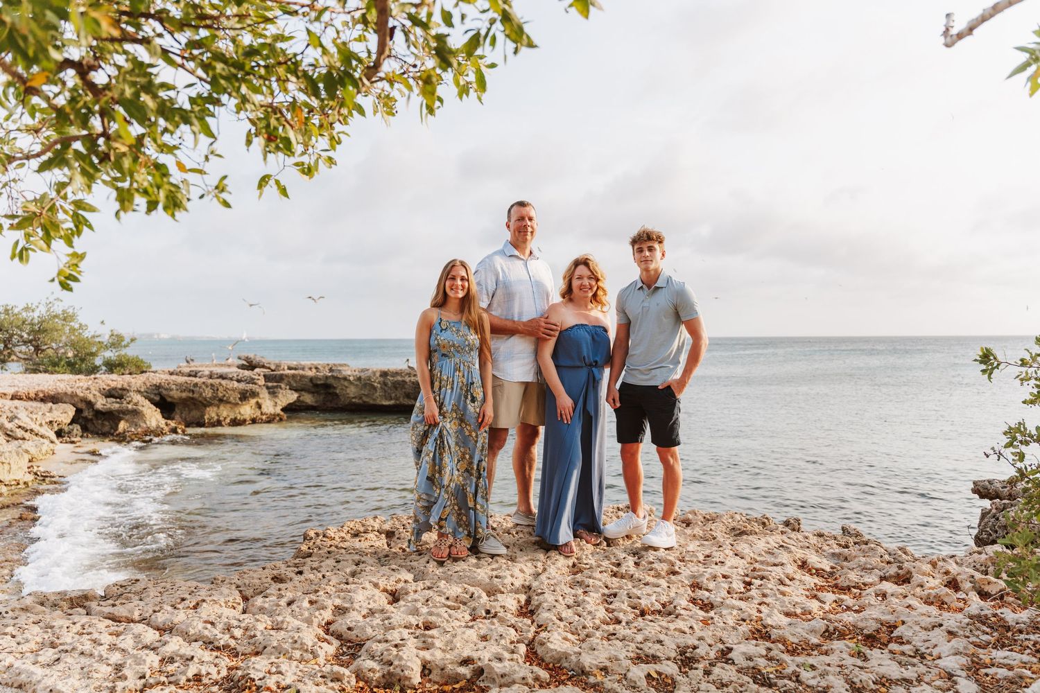 A group stands together on a rocky beach coastline during golden hour at sunset.