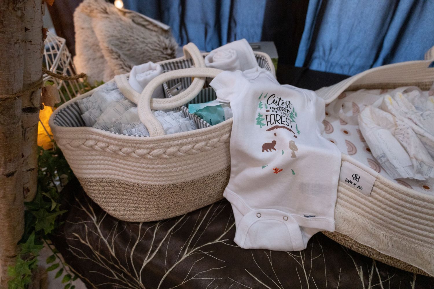 Woven rope baskets containing white baby clothes and shoes arranged on a rustic wooden surface.