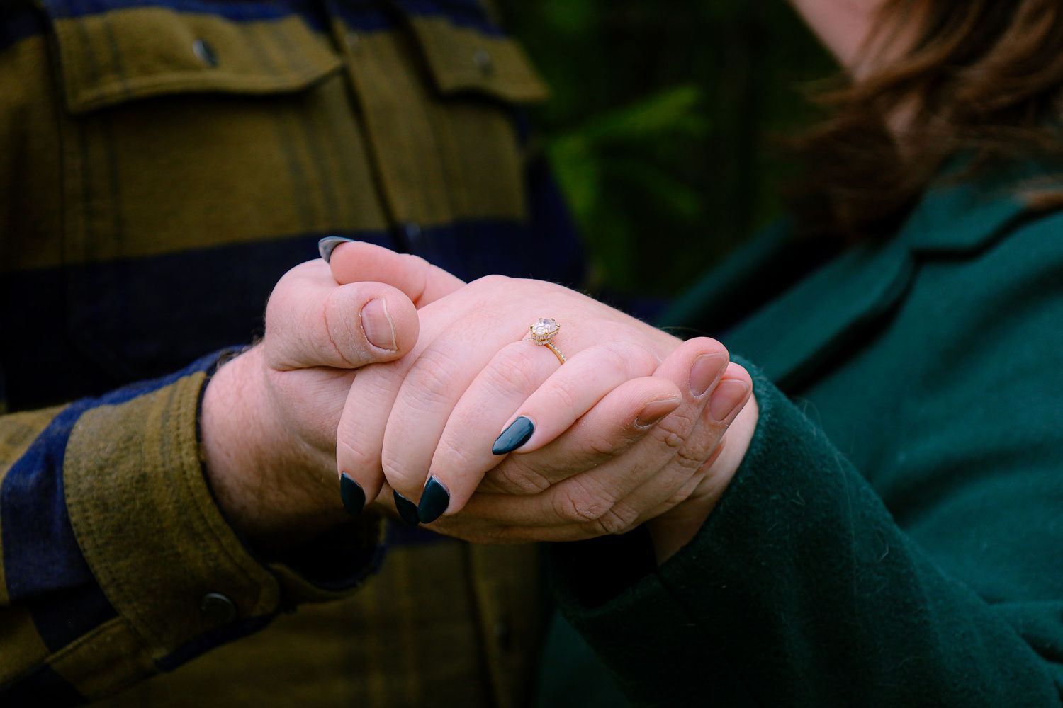 Two hands tenderly clasped together, with one person wearing a dark jacket and the other wearing a green sweater.