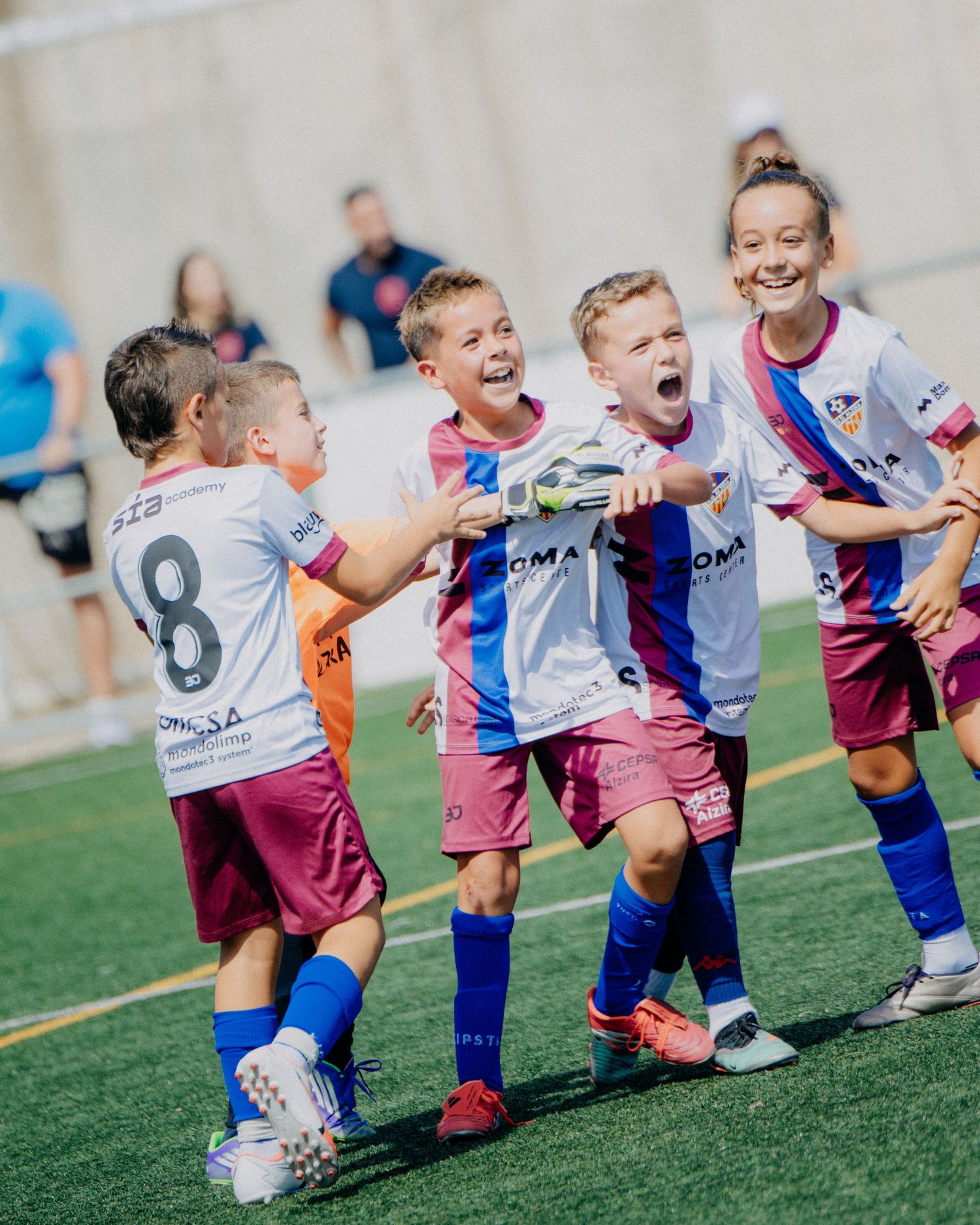 Joyful youth soccer players in white and pink uniforms celebrate a goal together.