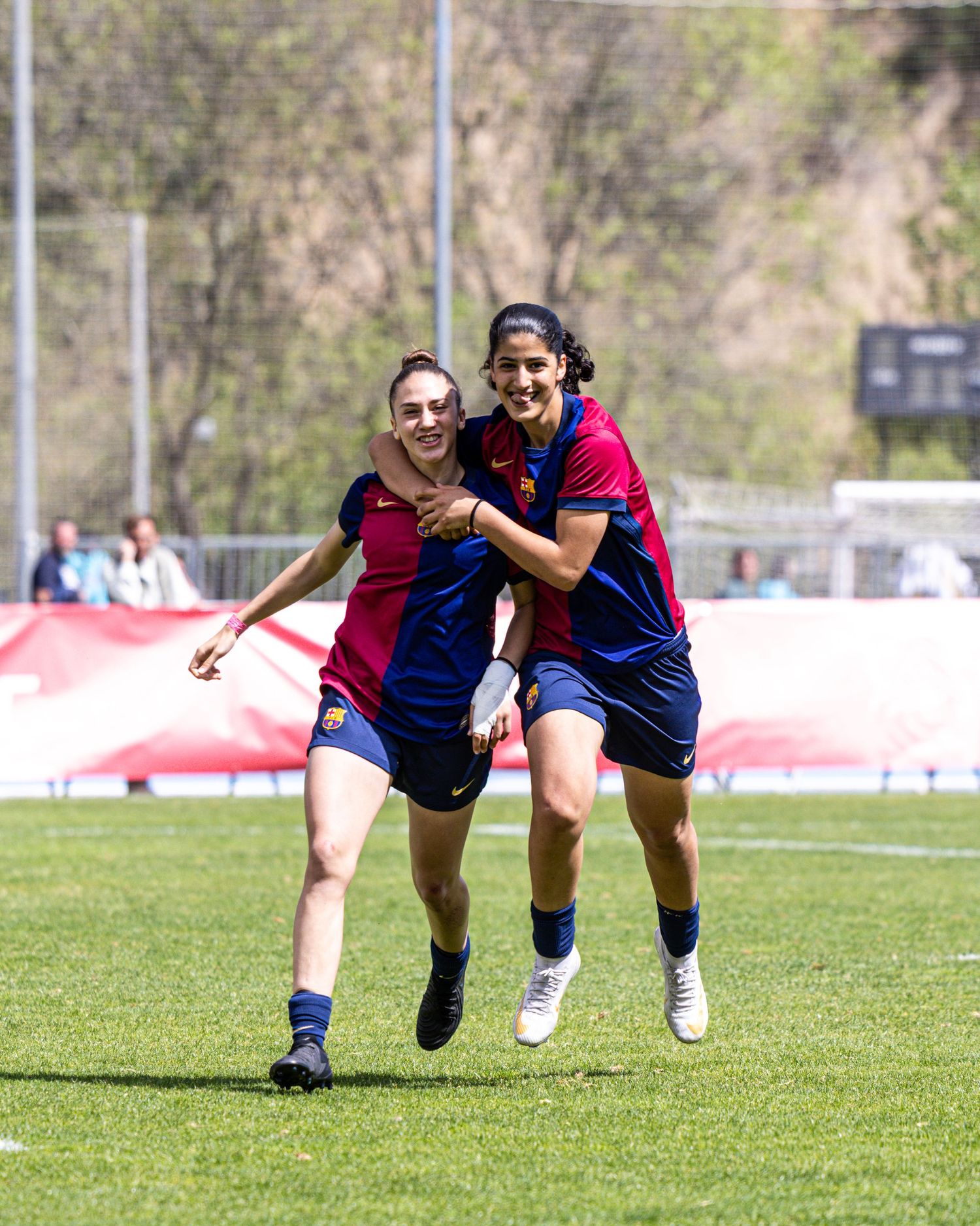 Two FC Barcelona women players celebrate joyfully on a sunny green soccer field.