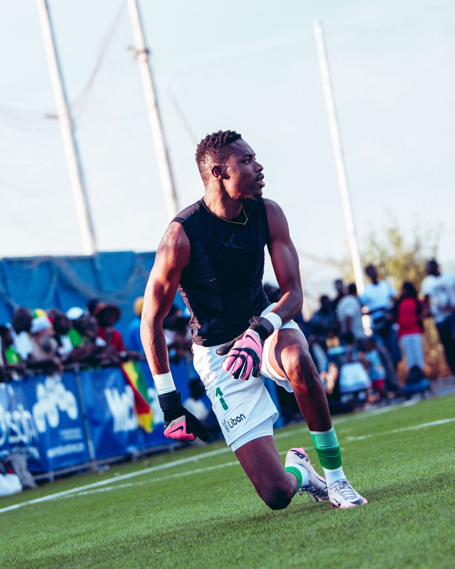 Athletic soccer player in black jersey kneels on green field during warm-up at an outdoor sports event.