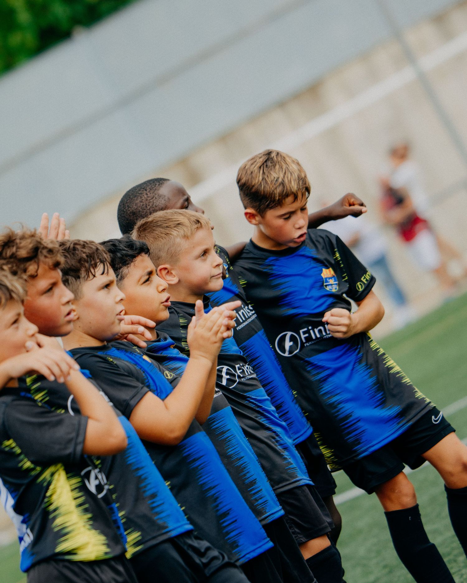 Group of young boys in black and blue soccer uniforms lined up and cheering on a sports field.