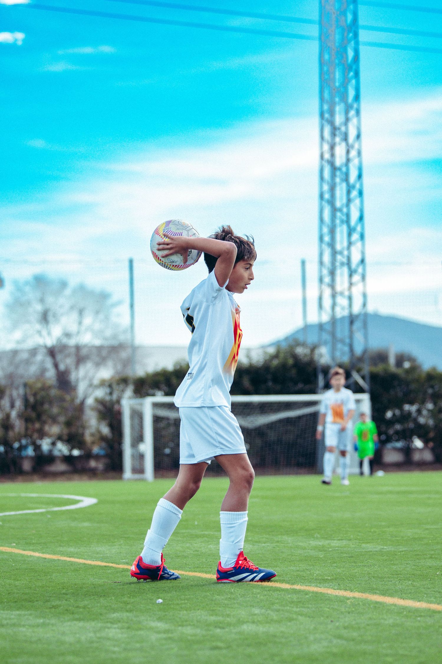 Youth soccer player in white kit prepares to take a throw-in during a match on green turf field.