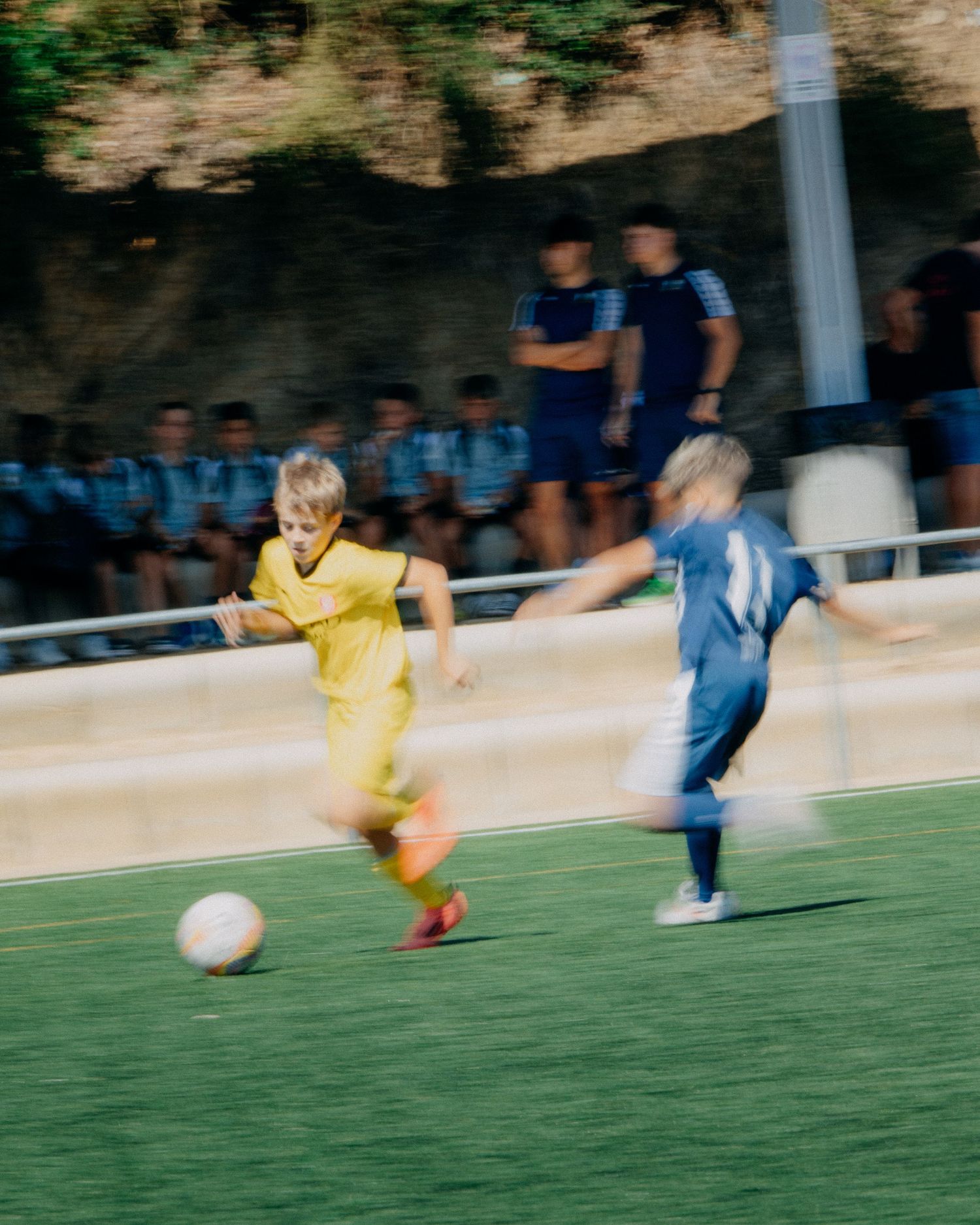 Motion blur action shot of two young boys in yellow and blue jerseys playing soccer on a grass field.
