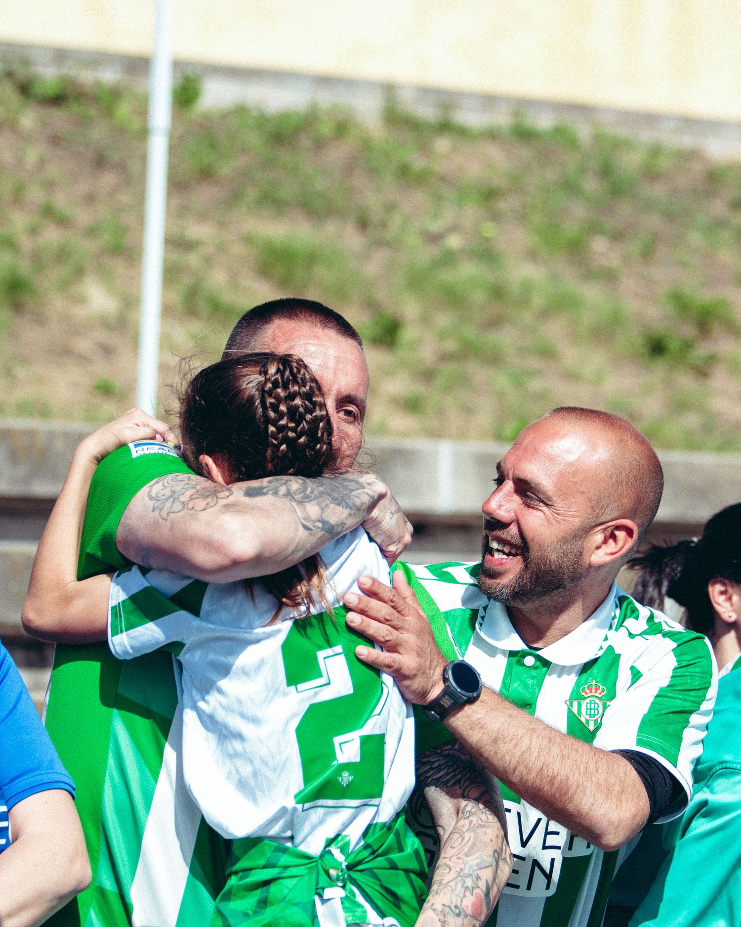 Three soccer players in green and white jerseys share an emotional embrace celebrating on the field.