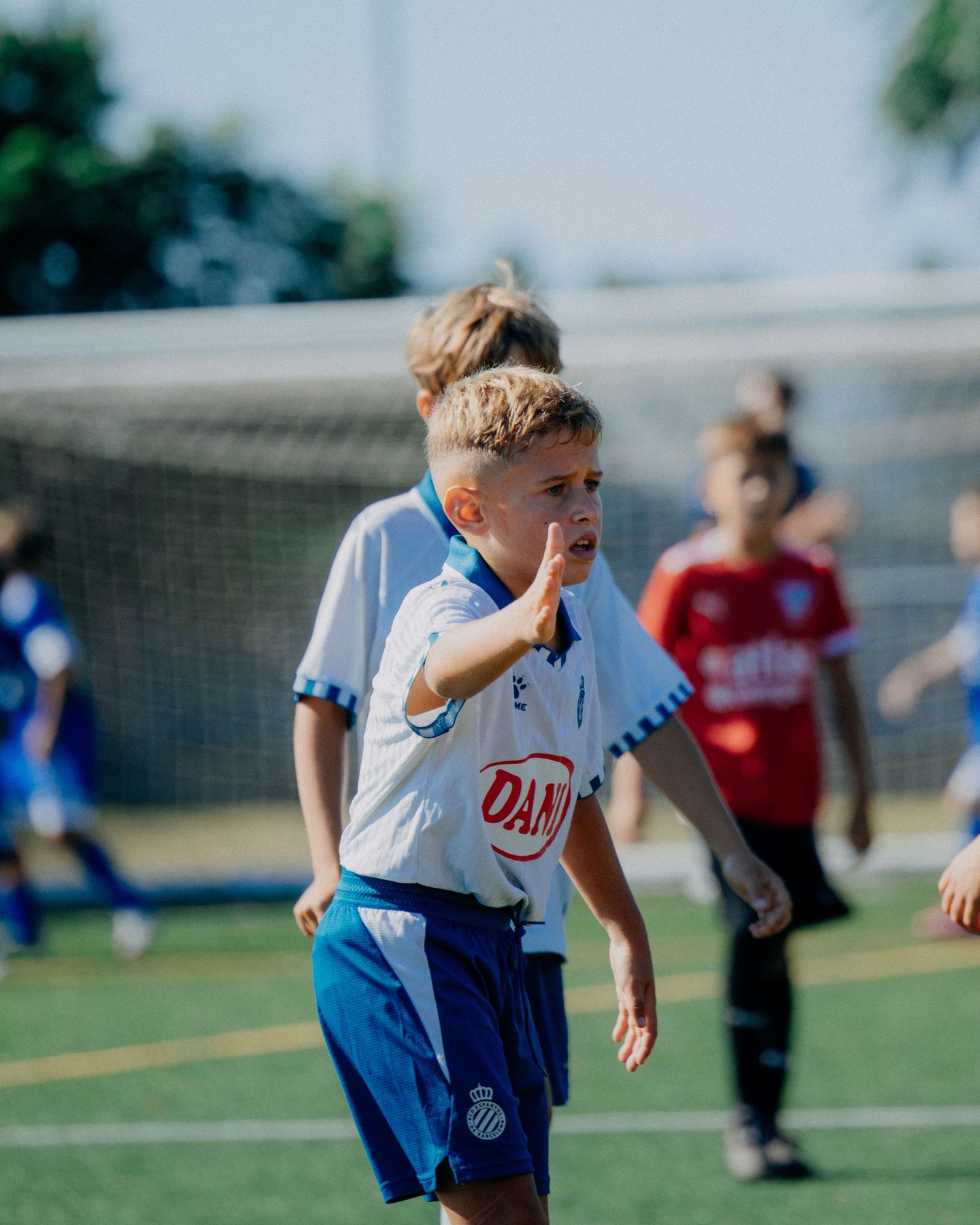 Young blonde soccer player in white Espanyol kit gestures during a youth match.