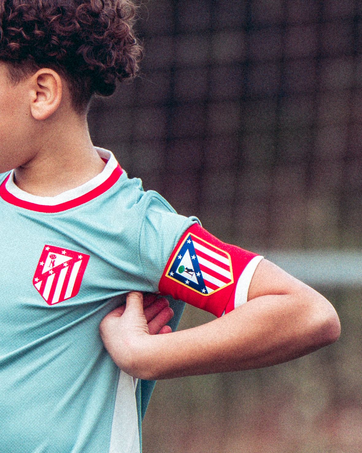 Close-up of young Atletico Madrid player wearing teal jersey and red club captain armband on field.