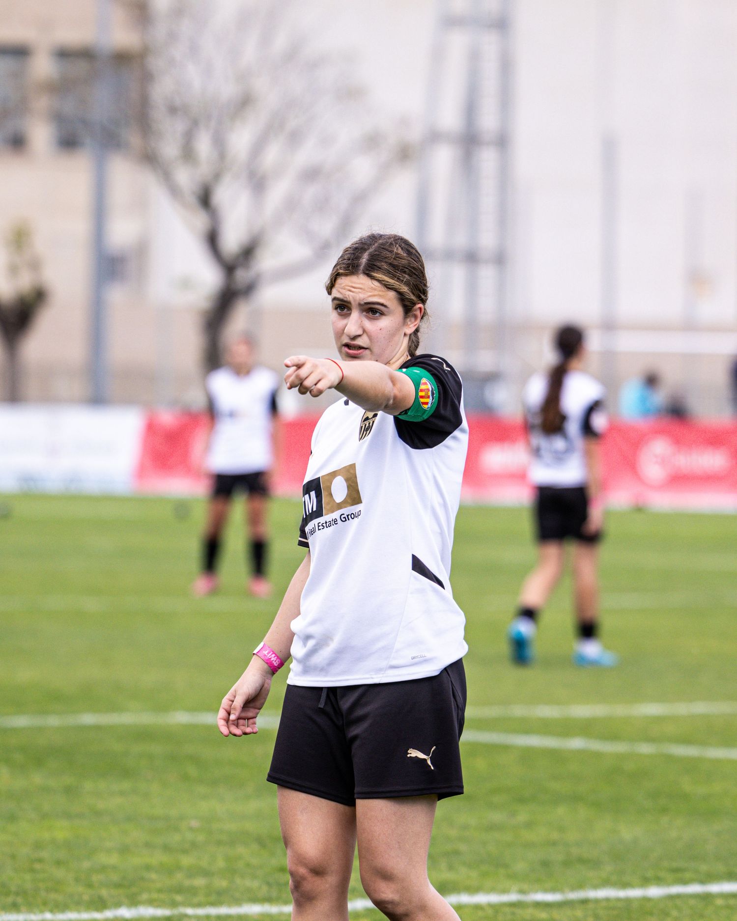 Female soccer player in white Puma kit points directions during a match on green field.