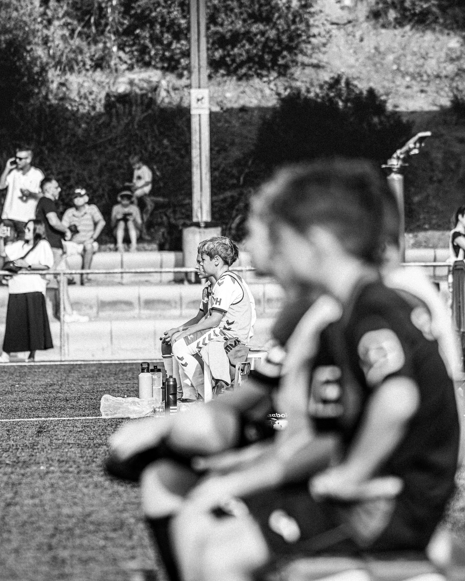 Black and white photo of spectators watching a youth soccer match from the sidelines.