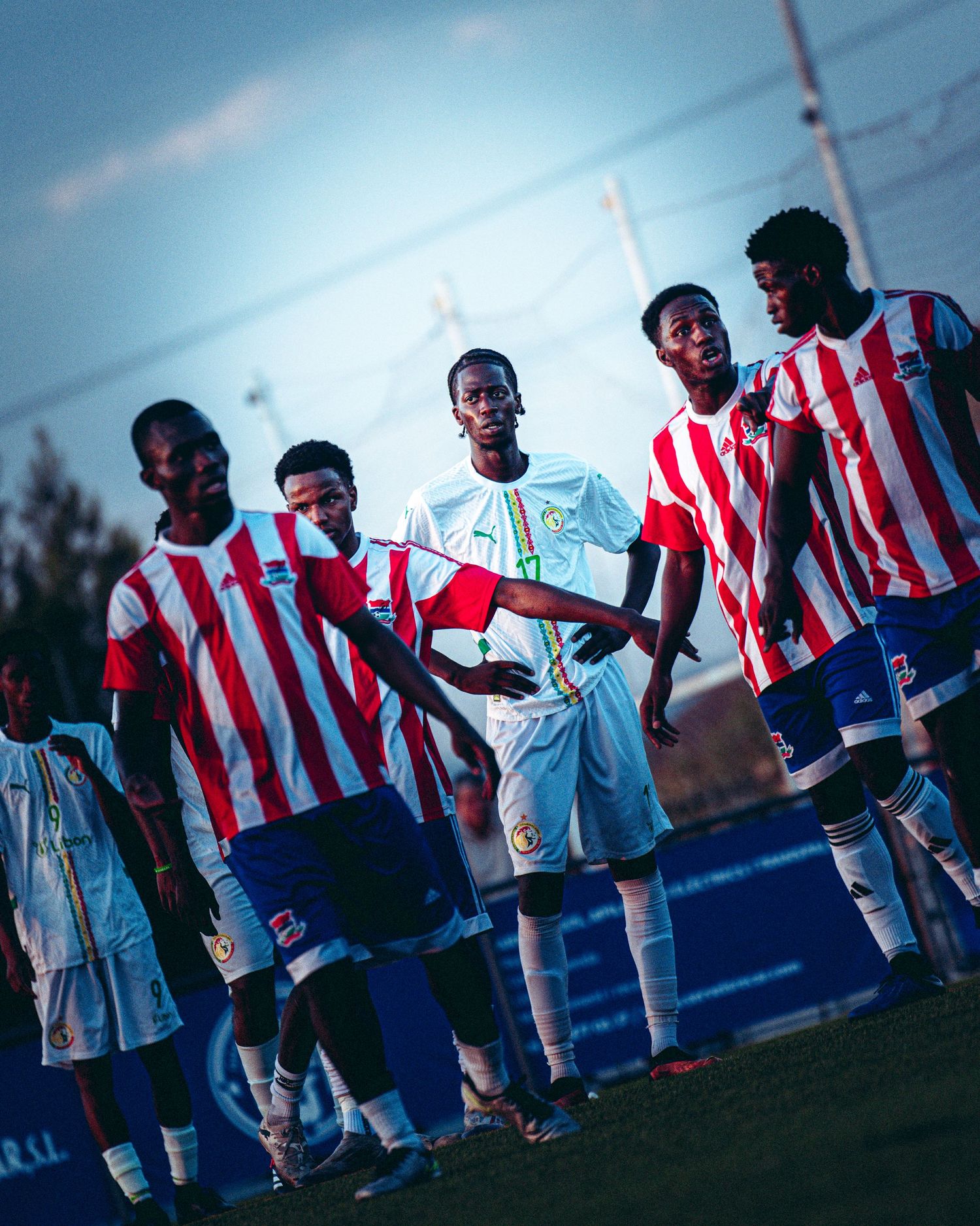 Young African soccer players in red and white striped jerseys gather on field at dusk.