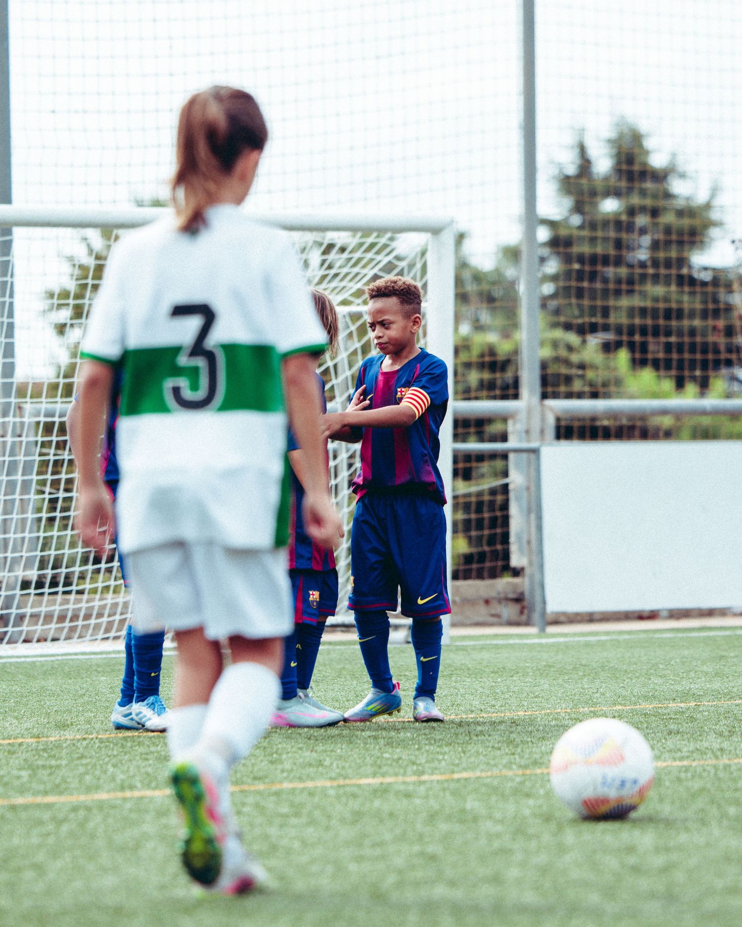 Young soccer player in FC Barcelona kit stands near goal during a youth match.