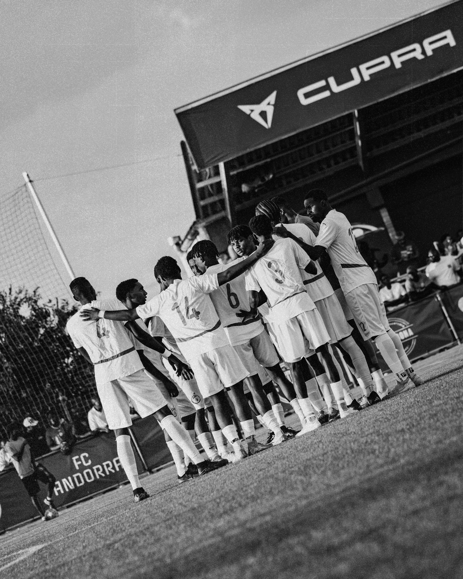 Black and white photo of youth soccer team huddling at FC Andorra Cupra stadium.