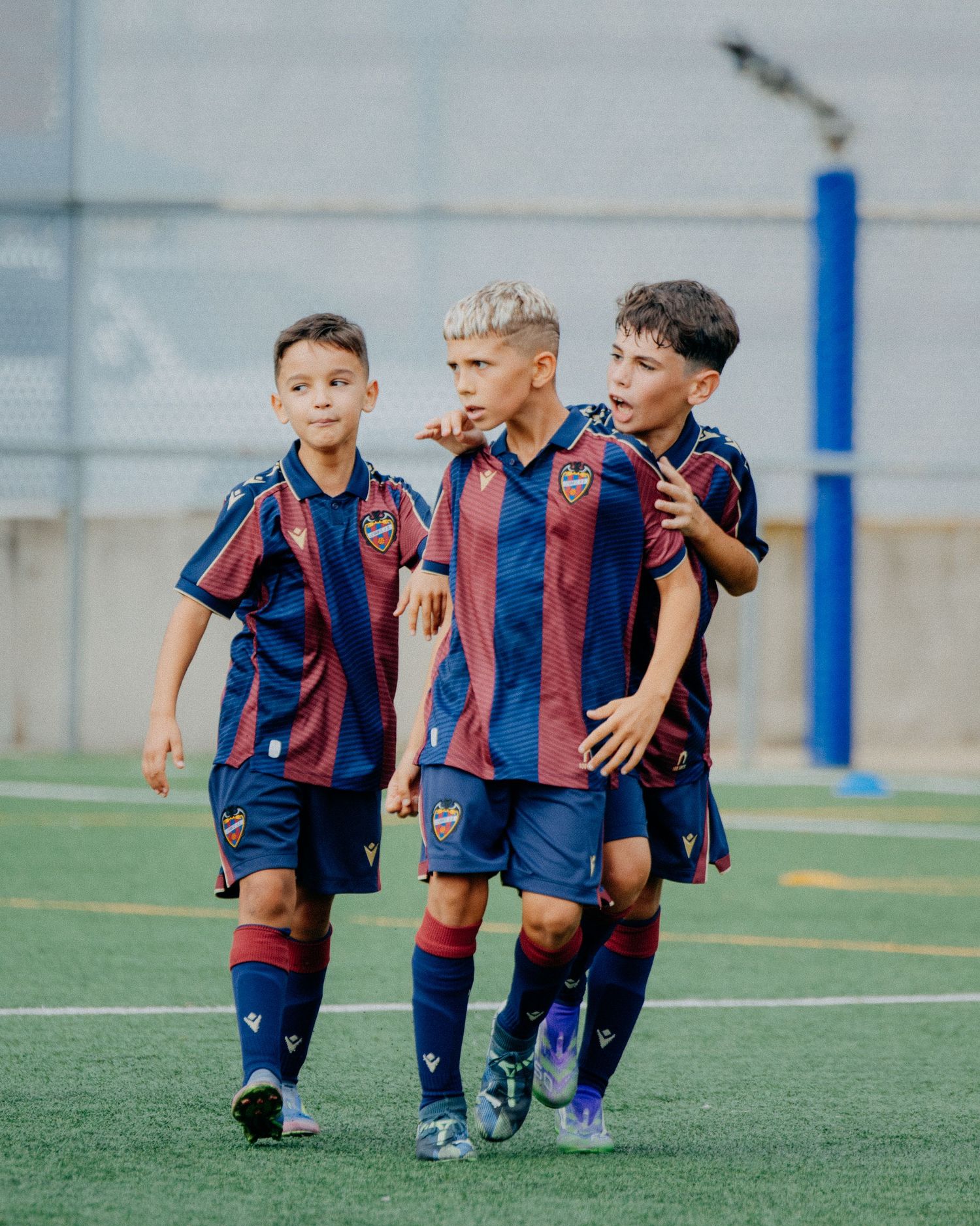 Three young soccer players in navy and red striped uniforms walk together on a field.