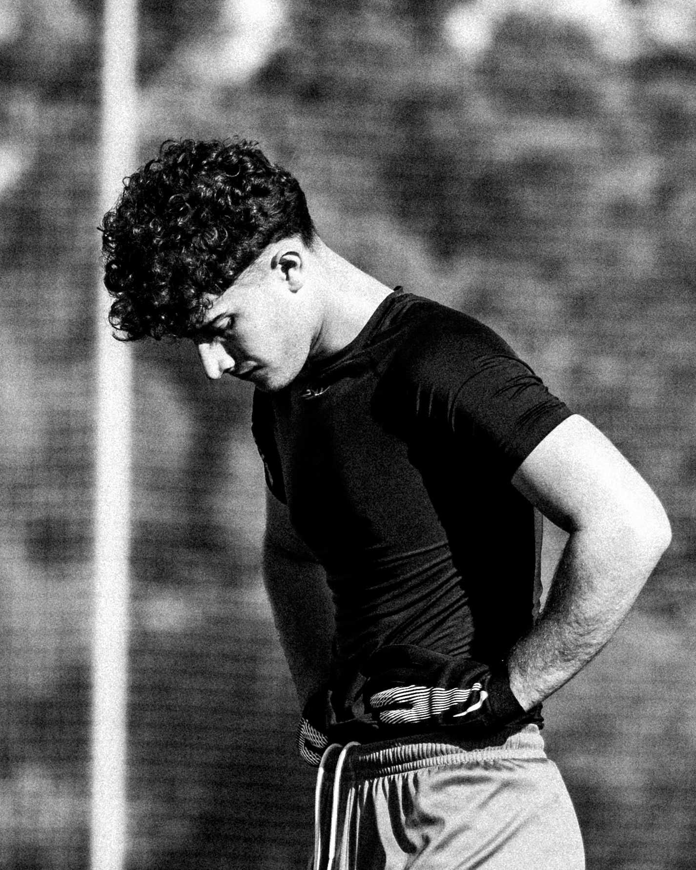 Curly-haired male soccer player looking down during training session in black and white.