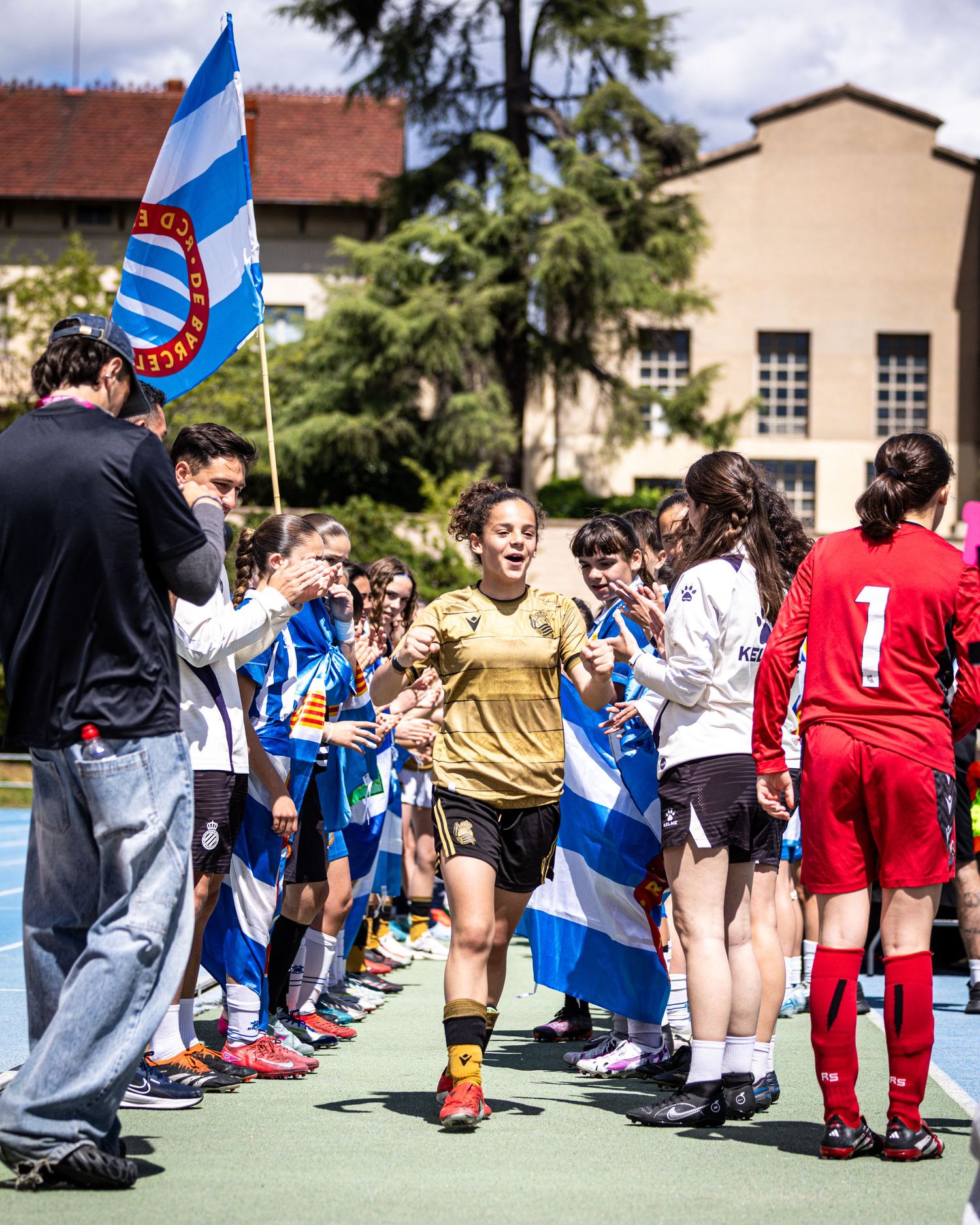 Female soccer player in gold kit runs through a guard of honor at a youth tournament.
