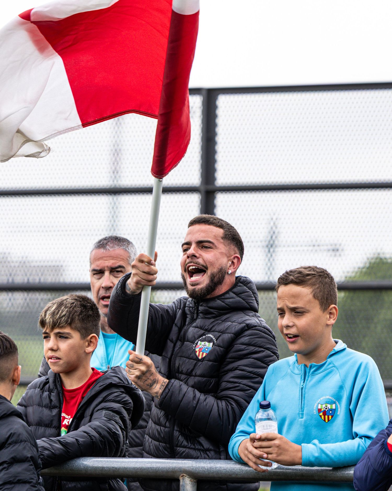 Passionate soccer fan waves red and white flag while cheering at youth football match.
