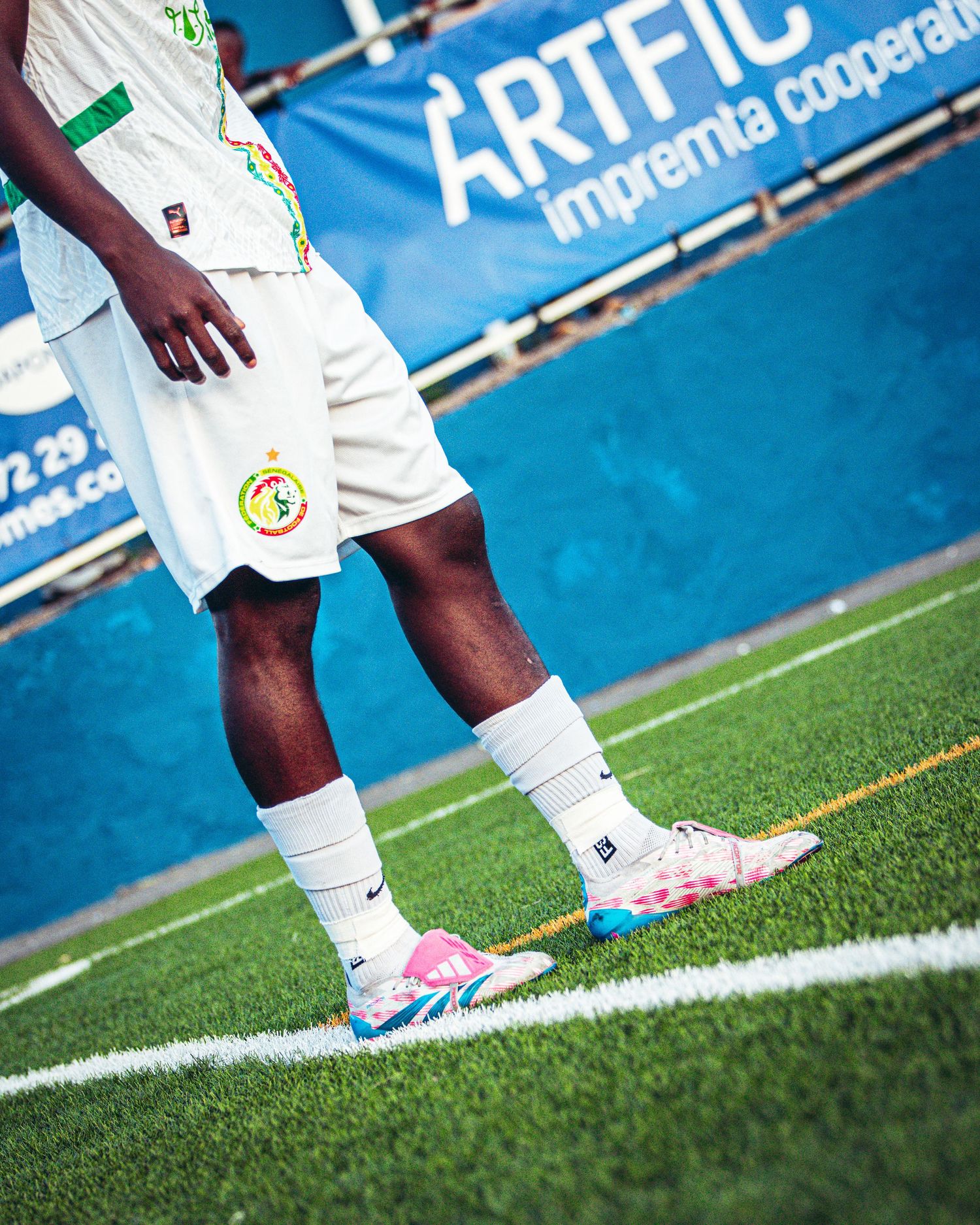 Close-up of soccer player wearing colorful pink blue Nike cleats on green turf field.