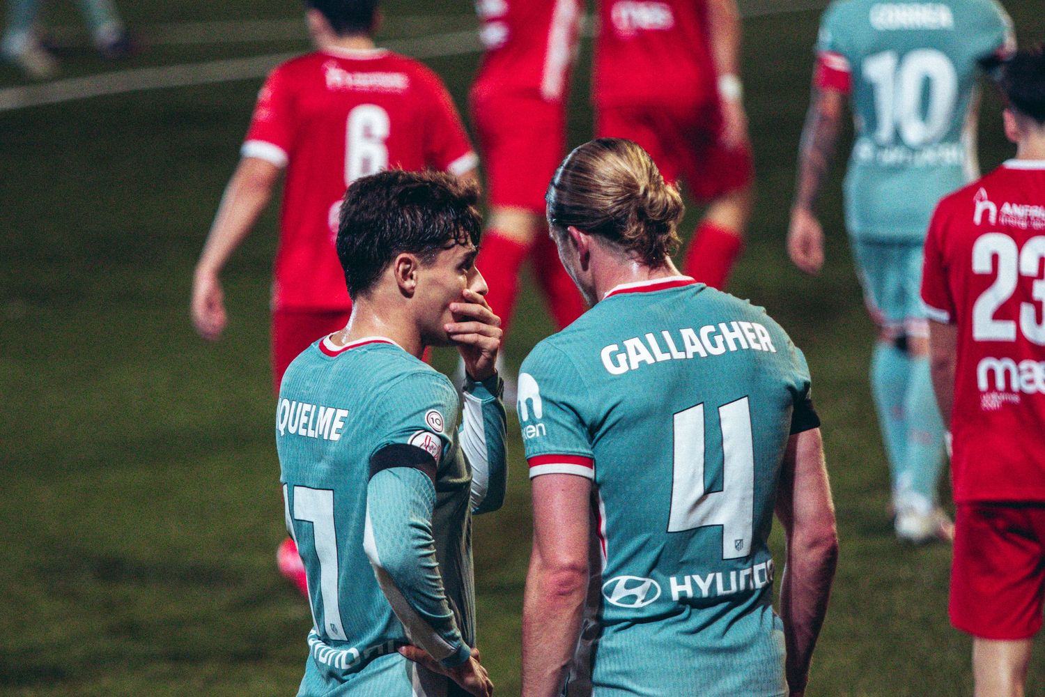 Atletico Madrid players Iquelme and Gallagher discuss tactics in teal away kit during professional soccer match.