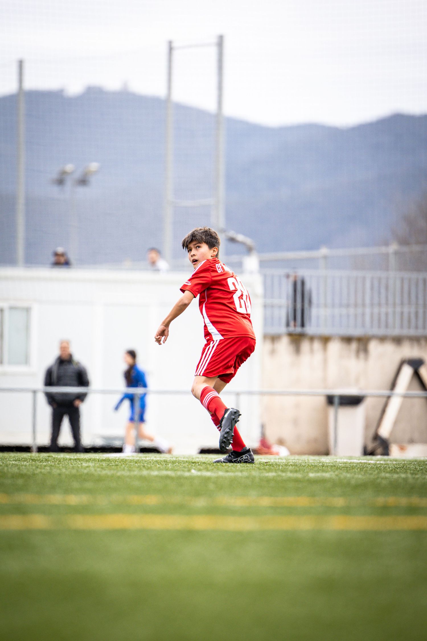 Young boy in red soccer uniform running on grass field during youth football match.