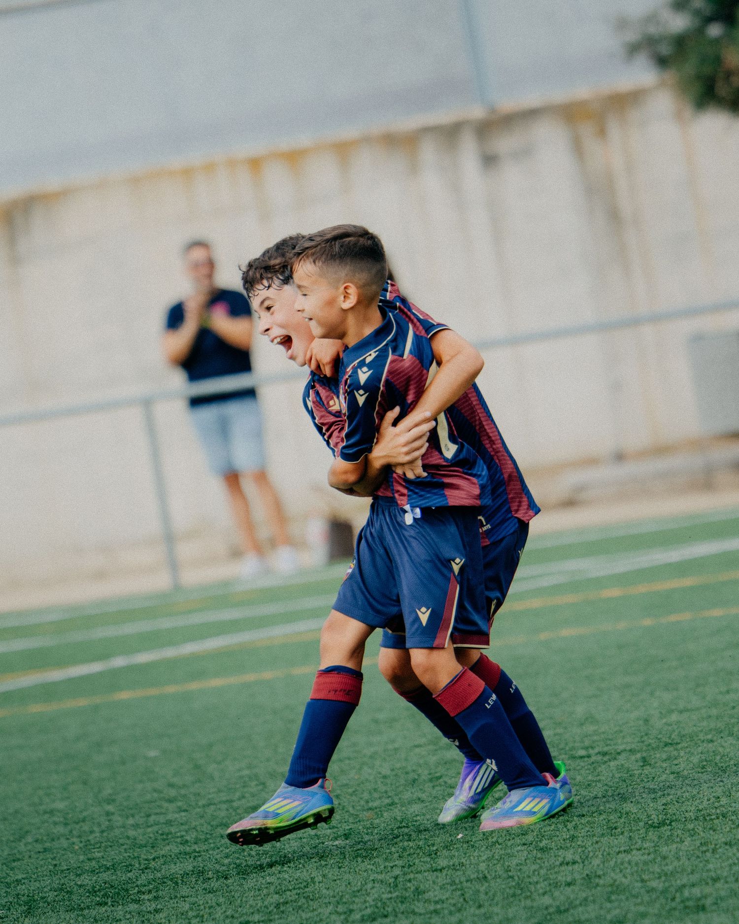 Two young boys in navy blue soccer uniforms celebrating a goal with excitement on the field.