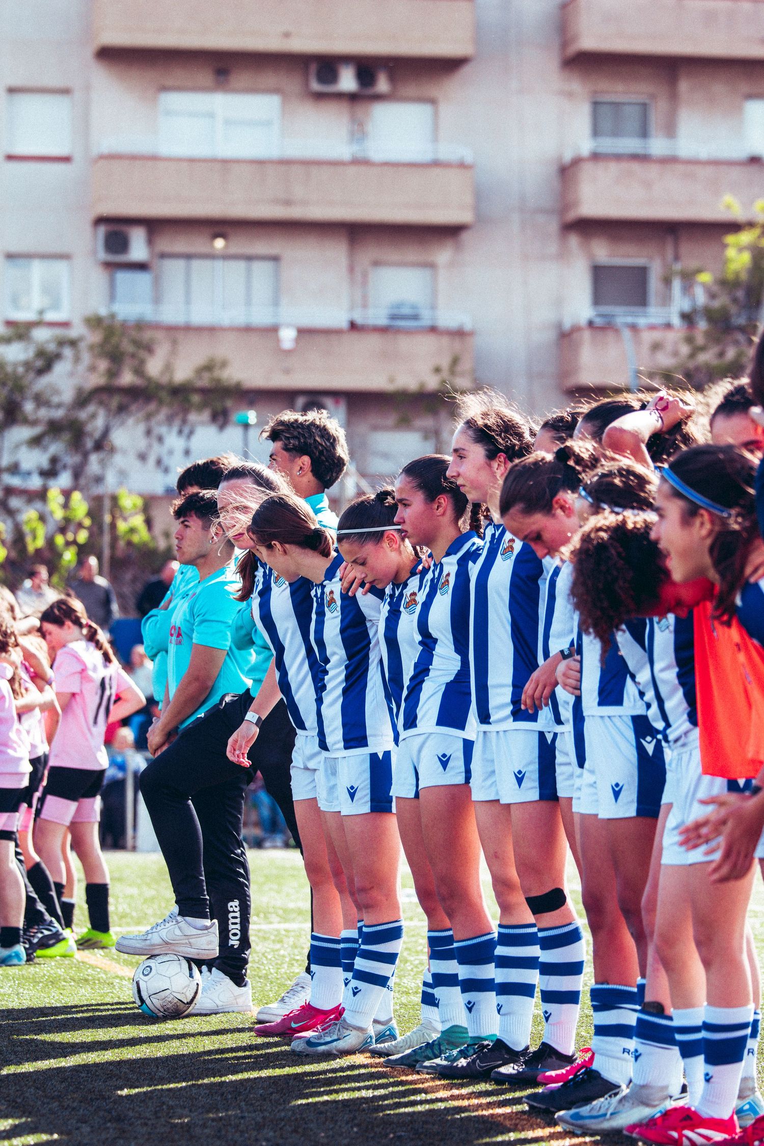 Female soccer team in blue and white uniforms lines up on field before a match.