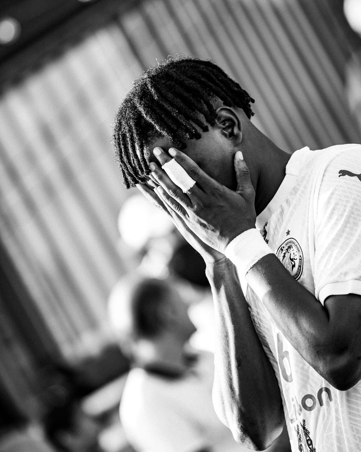 Black and white portrait of a young soccer player covering his face with his hands.